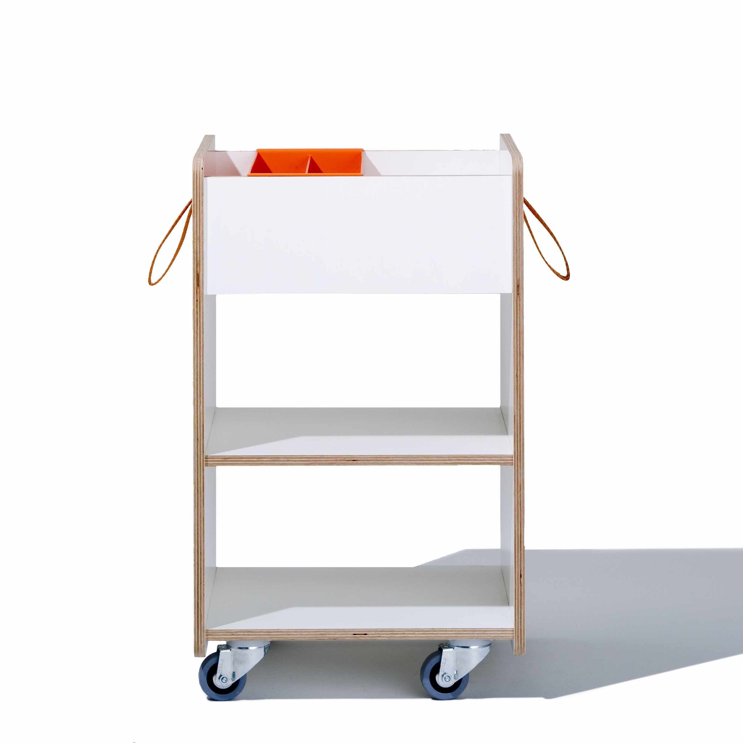 The Richard Lampert Trolley Fixx Kids features three white shelves with orange handles and dividers on a wooden structure, set on wheels. Pictured against a white background, it casts a shadow to the right.