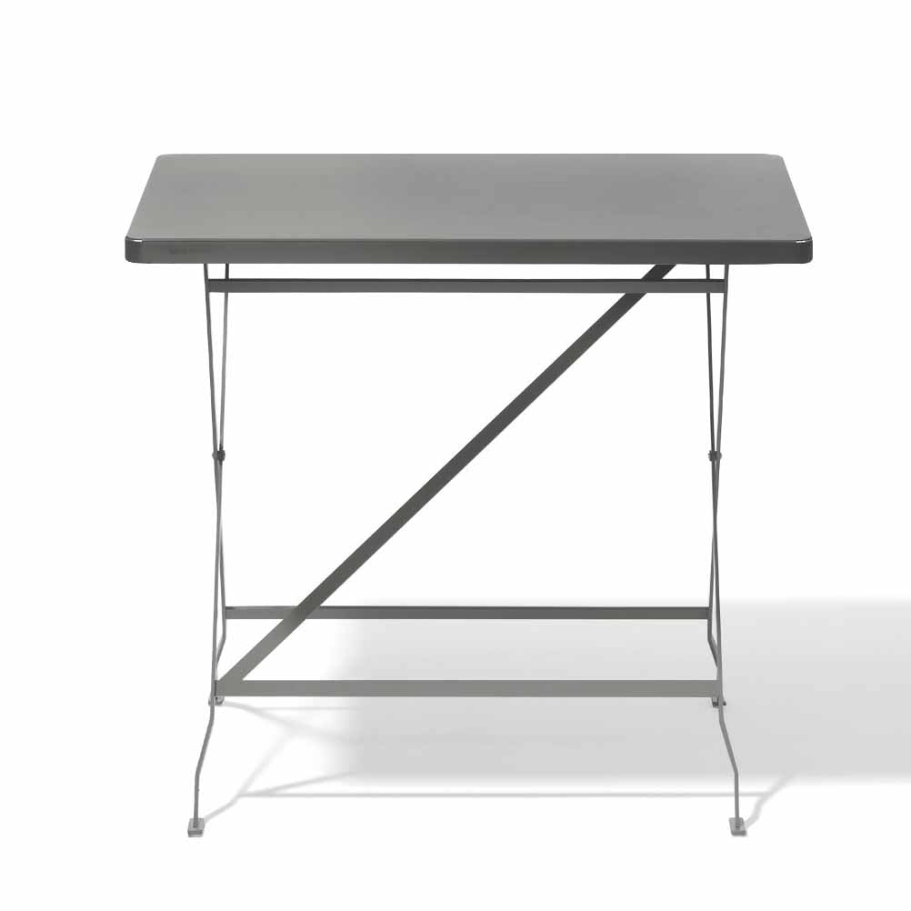The Flip Bistro Table by Richard Lampert is a minimalist gray dining table with a rectangular stainless steel top and slender legs forming a simple geometric design. A shadow on the right indicates left-side lighting, showcasing the brands timeless style.