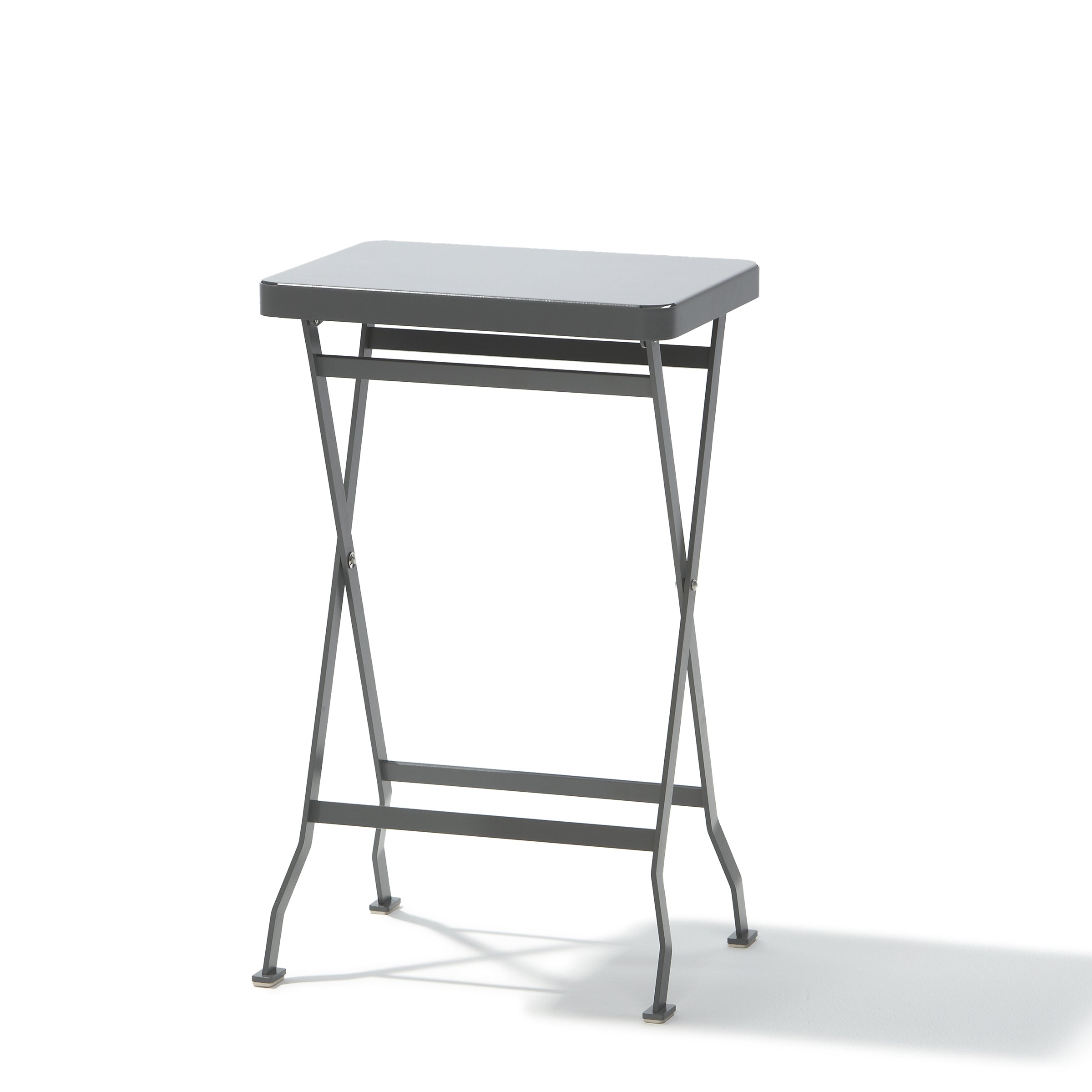 The Flip Side Table by Richard Lampert, a premium quality folding table, features thin stainless steel legs and a simple design with crossed supports beneath its top. The small, gray table is set against a plain white background.
