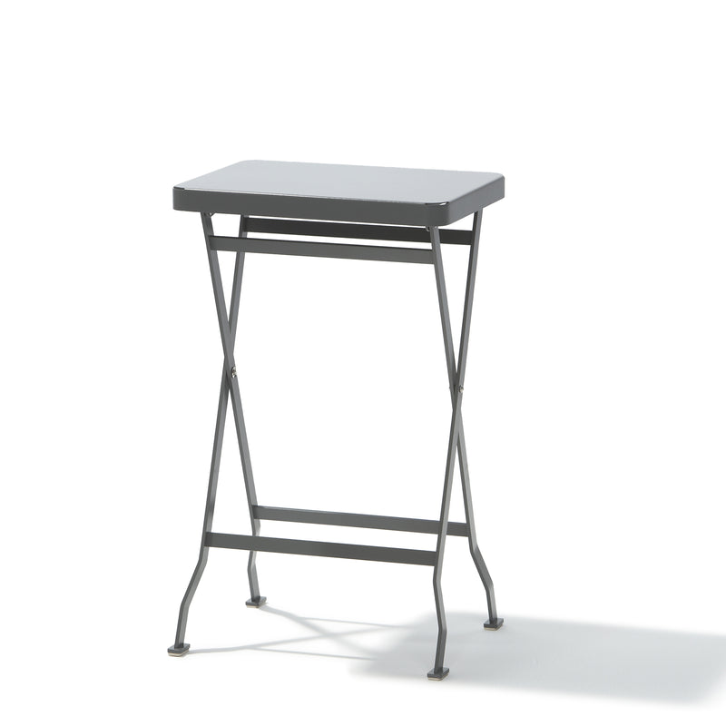 The Flip Side Table by Richard Lampert, a premium quality folding table, features thin stainless steel legs and a simple design with crossed supports beneath its top. The small, gray table is set against a plain white background.