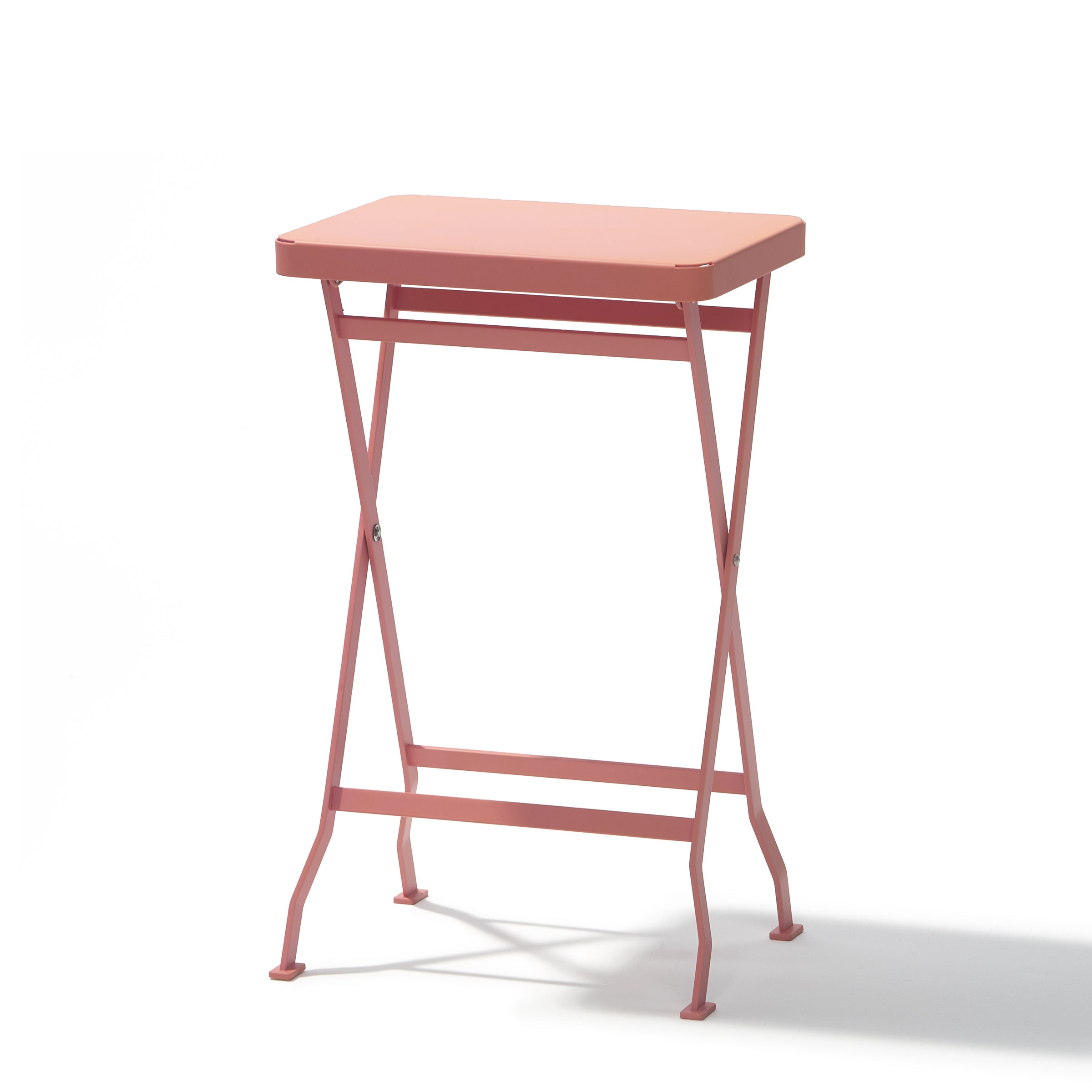 The Flip Side Table by Richard Lampert is a small, rectangular, pink folding table with a flat top and thin crossed legs, made from premium quality stainless steel. It sits against a plain white background, casting a faint shadow beneath it.