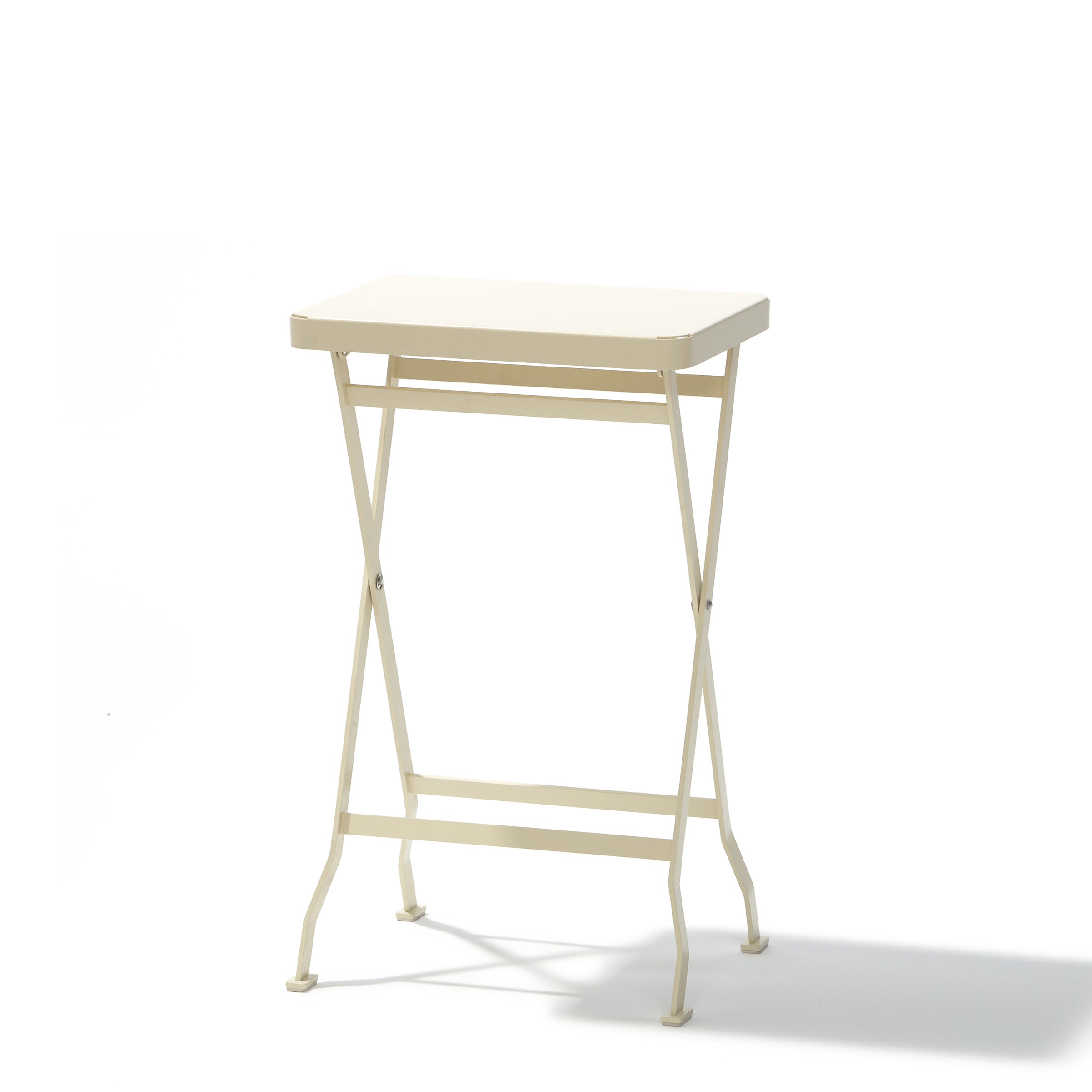 The Flip Side Table by Richard Lampert is a small, cream-colored folding table with a rectangular top and crossed legs. Its simple frame and premium quality make it a minimalistic and portable design perfect for any setting. It stands elegantly against a white background.