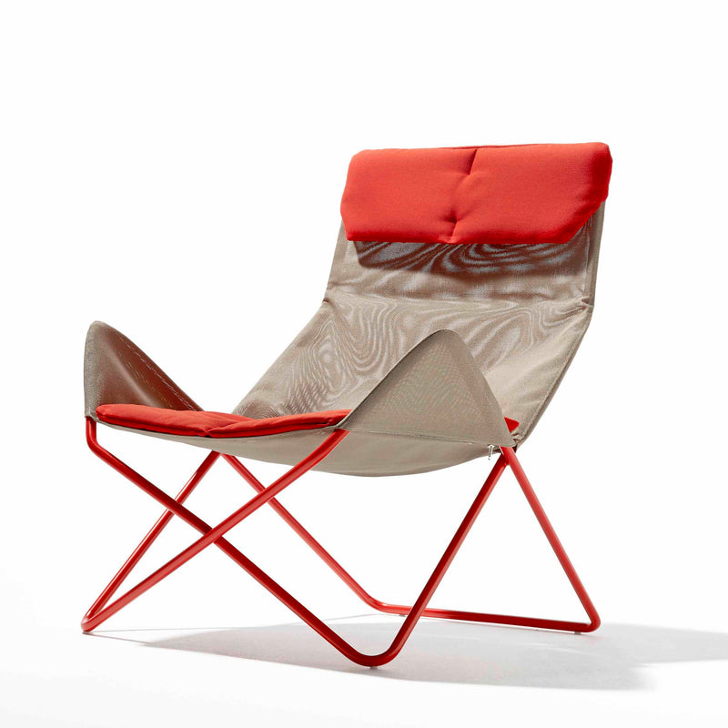 The In-Out Chair by Richard Lampert is a modern lounge chair ideal for outdoor use. It features a red cushioned seat and headrest, beige mesh backrest, weather-resistant red metal frame, and X-shaped legs for a sleek design against a white background.