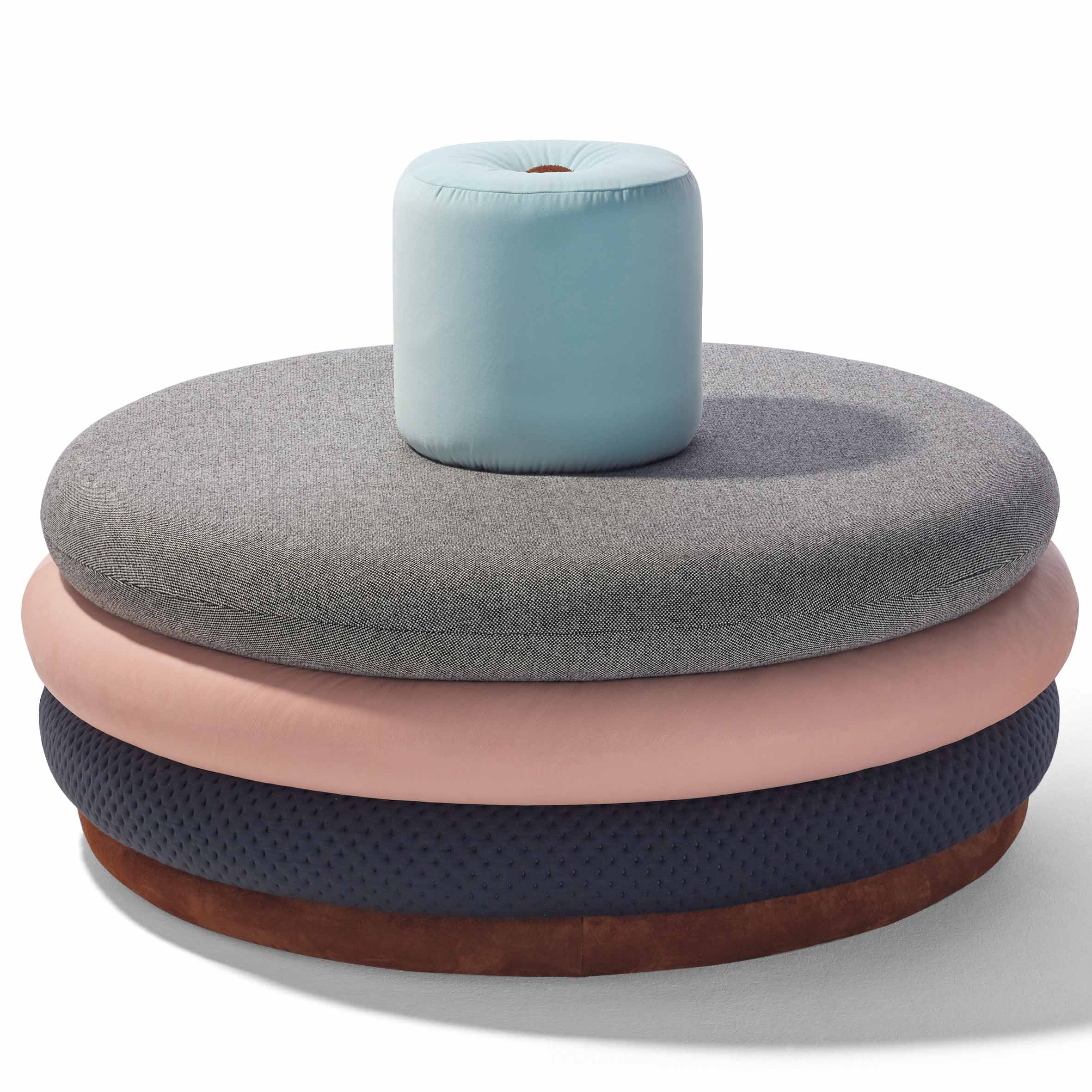 Introducing Richard Lamperts Island Tom: a circular, multi-layered ottoman with four stacked cushions in light gray, soft pink, dark blue, and brown. Topped with a turquoise cushion for personalized style and comfort.