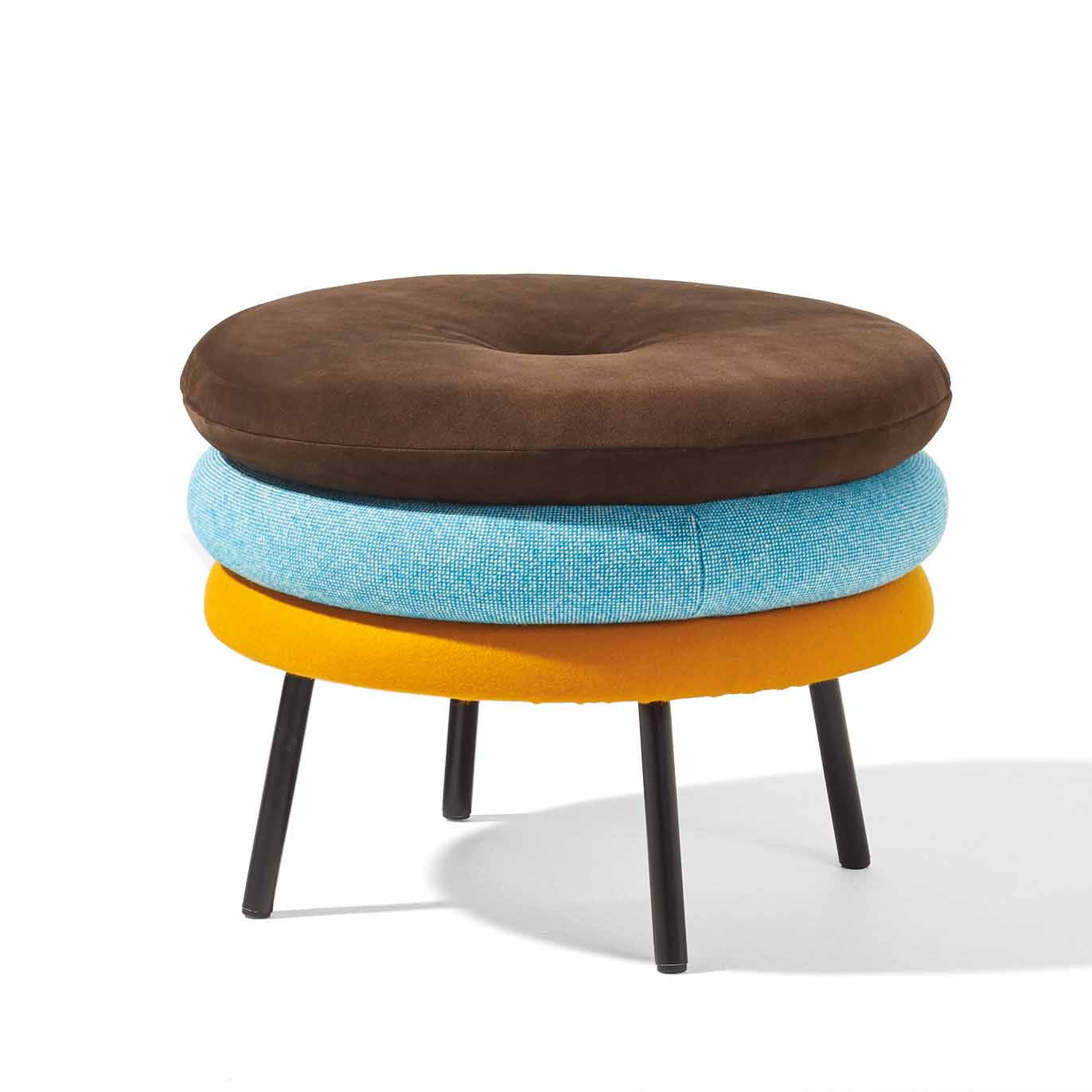 Meet the Richard Lampert Little Tom Stool, a contemporary piece with three stacked cushioned layers in brown, blue, and yellow. It stands on sleek black metal legs and casts a rightward shadow against a white backdrop.