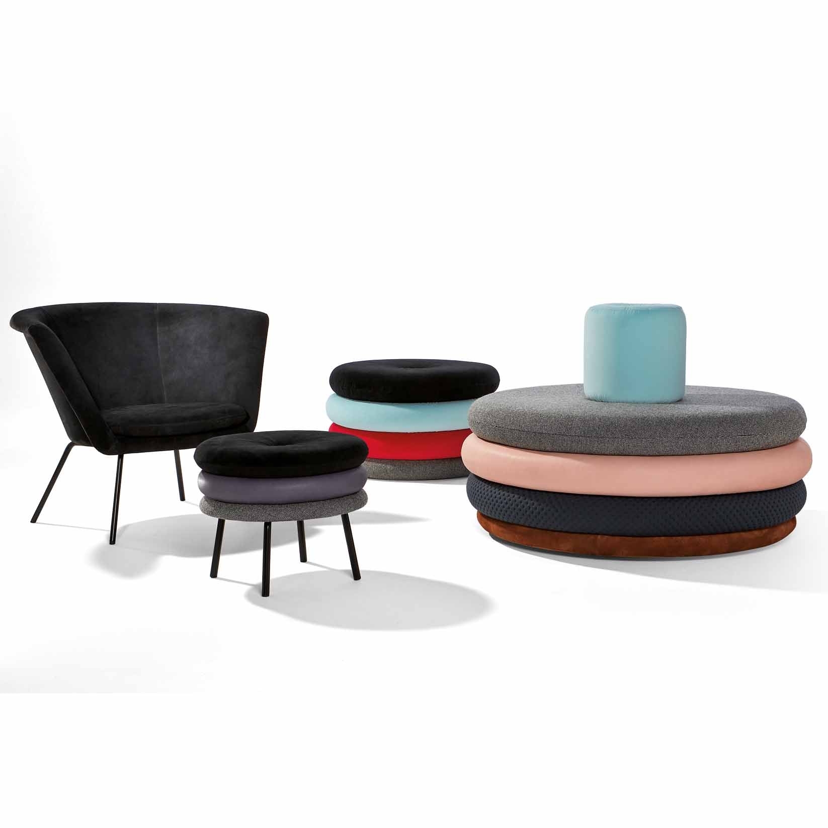 The modern furniture collection includes a black velvet chair with thin legs, a small matching footrest, and colorful stacked ottoman cushions on sleek black legs. The Richard Lampert Little Tom Stool completes the ensemble with its playful yet sophisticated charm.
