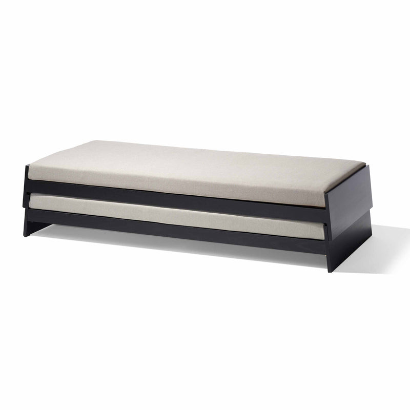 The Lönneberga Stacking Bed by Richard Lampert features a sleek dark wooden frame with a light beige mattress. Its minimalist, space-saving design and low-profile flat headboard make it a versatile addition to any room, embodying contemporary style and functionality.