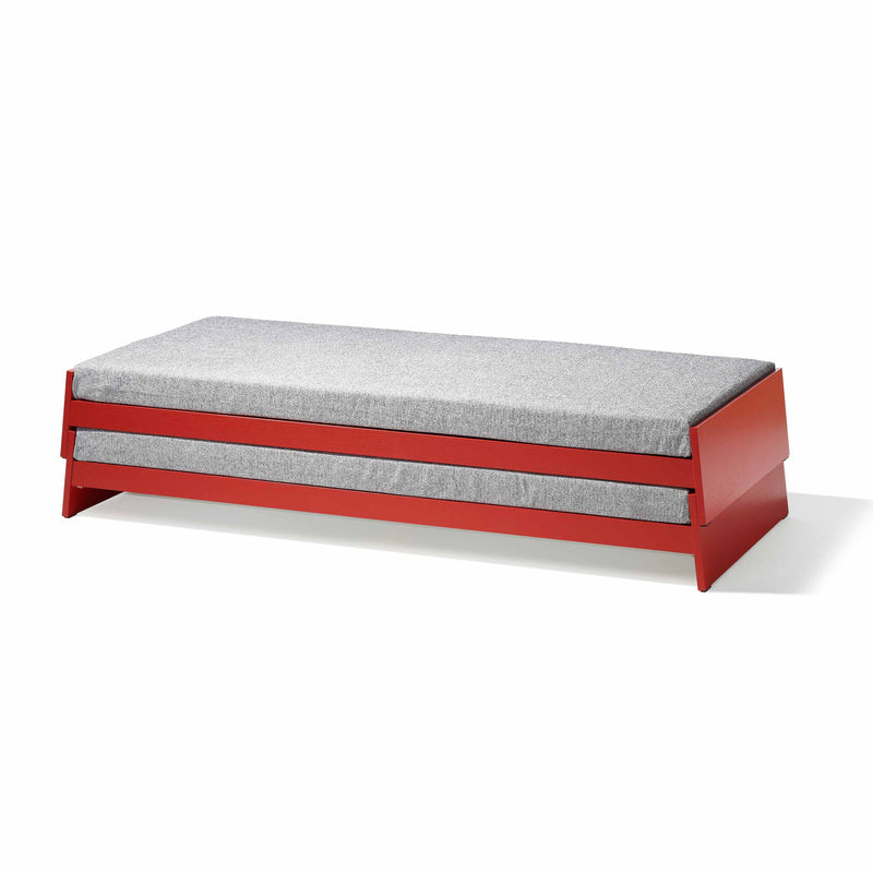 The Lönneberga Stacking Bed by Richard Lampert is a modern, minimalist daybed with a red wooden frame and a simple gray cushion, shown against a plain white background.