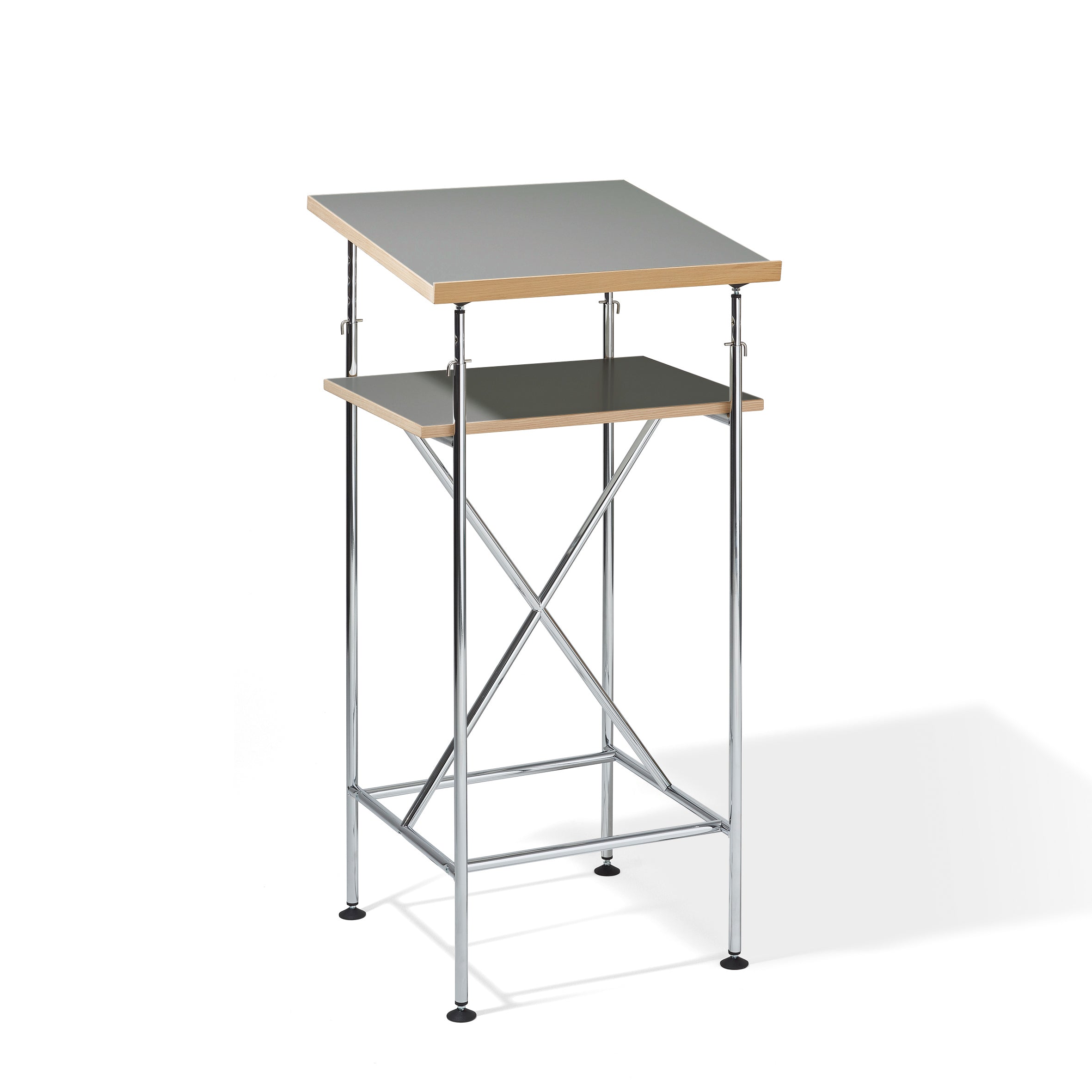 The Milla High Desk by Richard Lampert is a two-tier drafting table inspired by the Eiermann design, featuring a metal frame with adjustable gray tabletops. The top surface angles slightly, while the lower shelf stays flat. It includes stability-enhancing crossbars and legs finished with black feet.