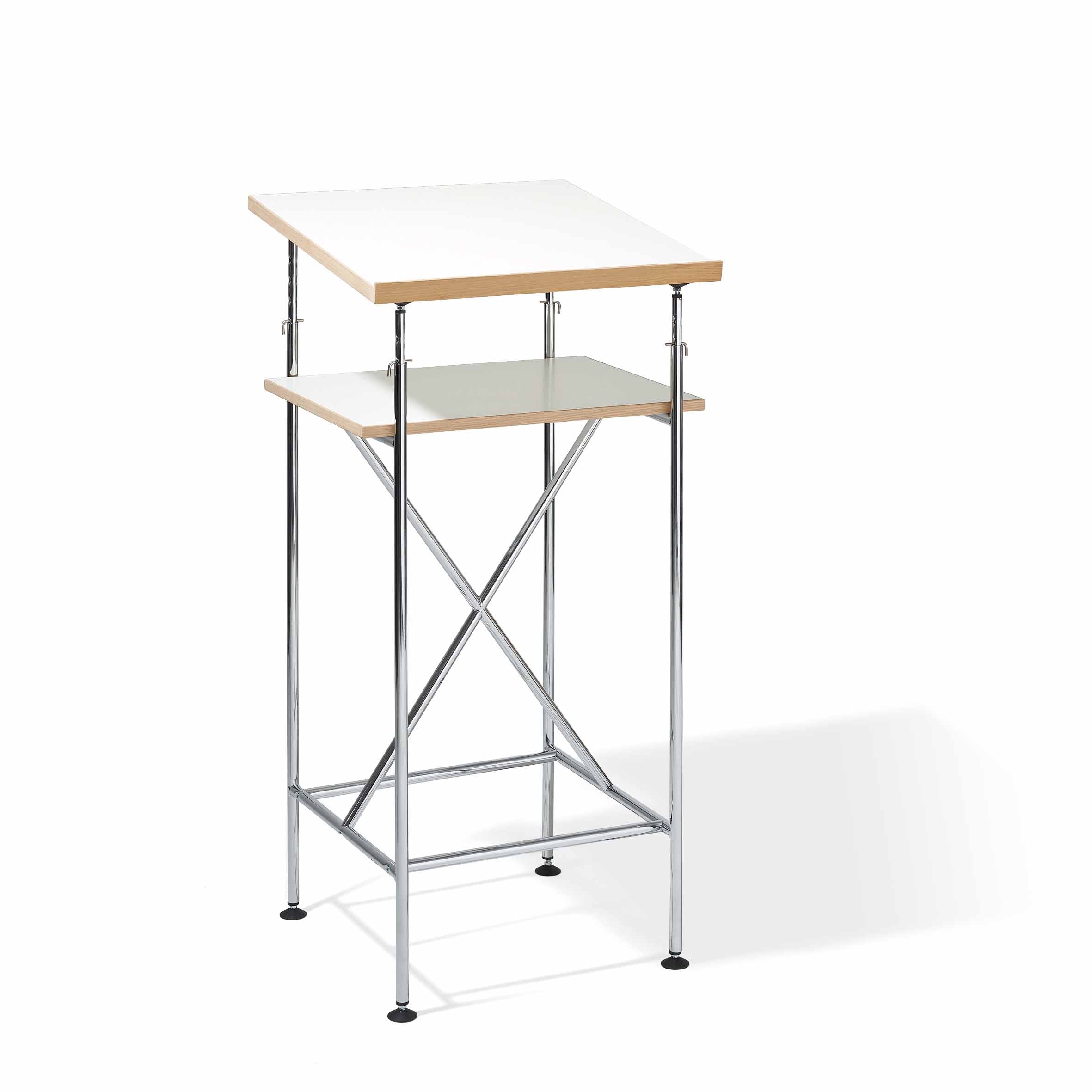 The Milla High Desk by Richard Lampert showcases a modern, minimalist design with a white top and smaller lower shelf. It features thin chrome crossbar legs and a light wood edge, making it perfect for active sitting and standing in various workspaces.