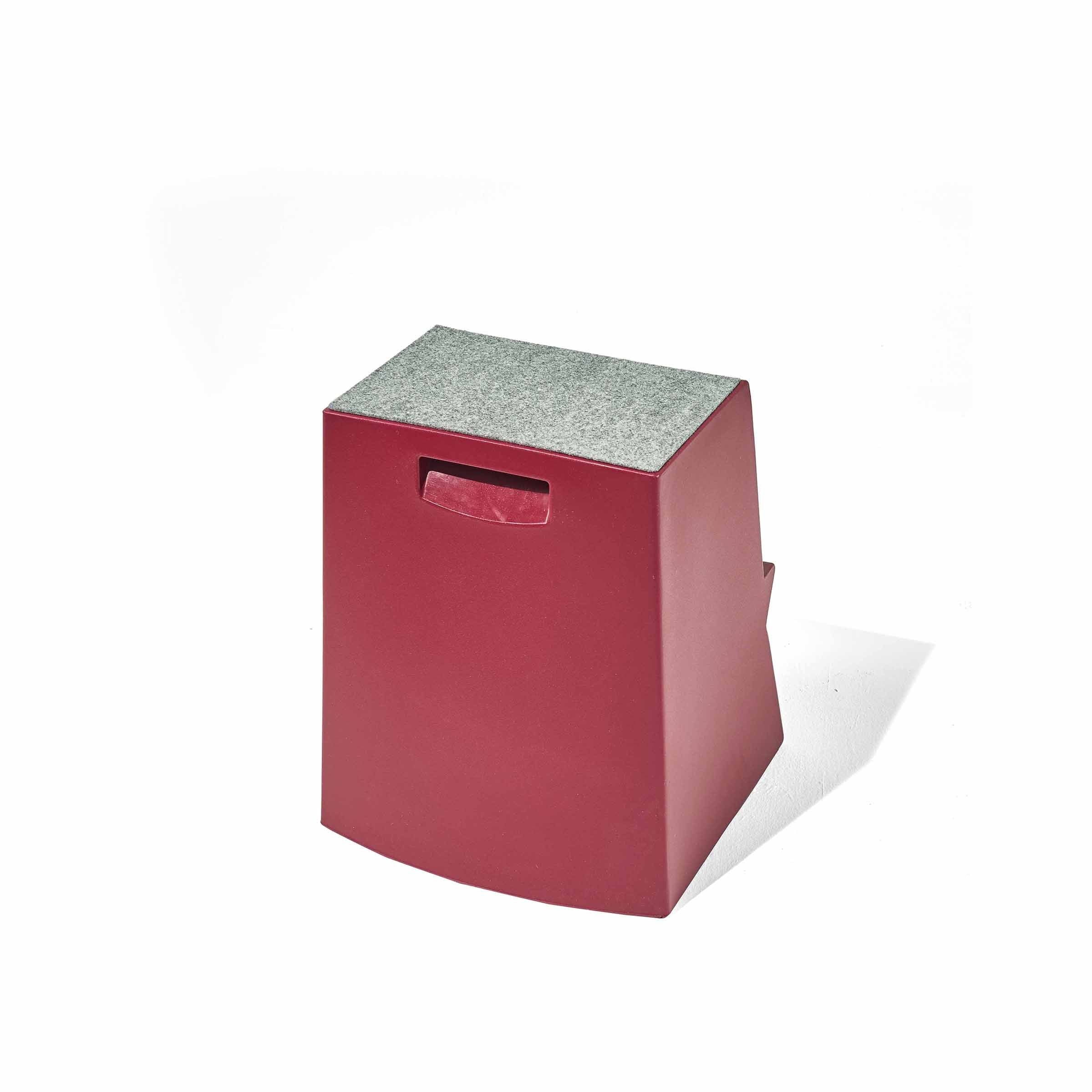 Richard Lamperts Mono Stepstool is red and trapezoidal, crafted from recyclable polyethylene. It has a gray top, a handle cutout on one side, and is showcased on a white background.