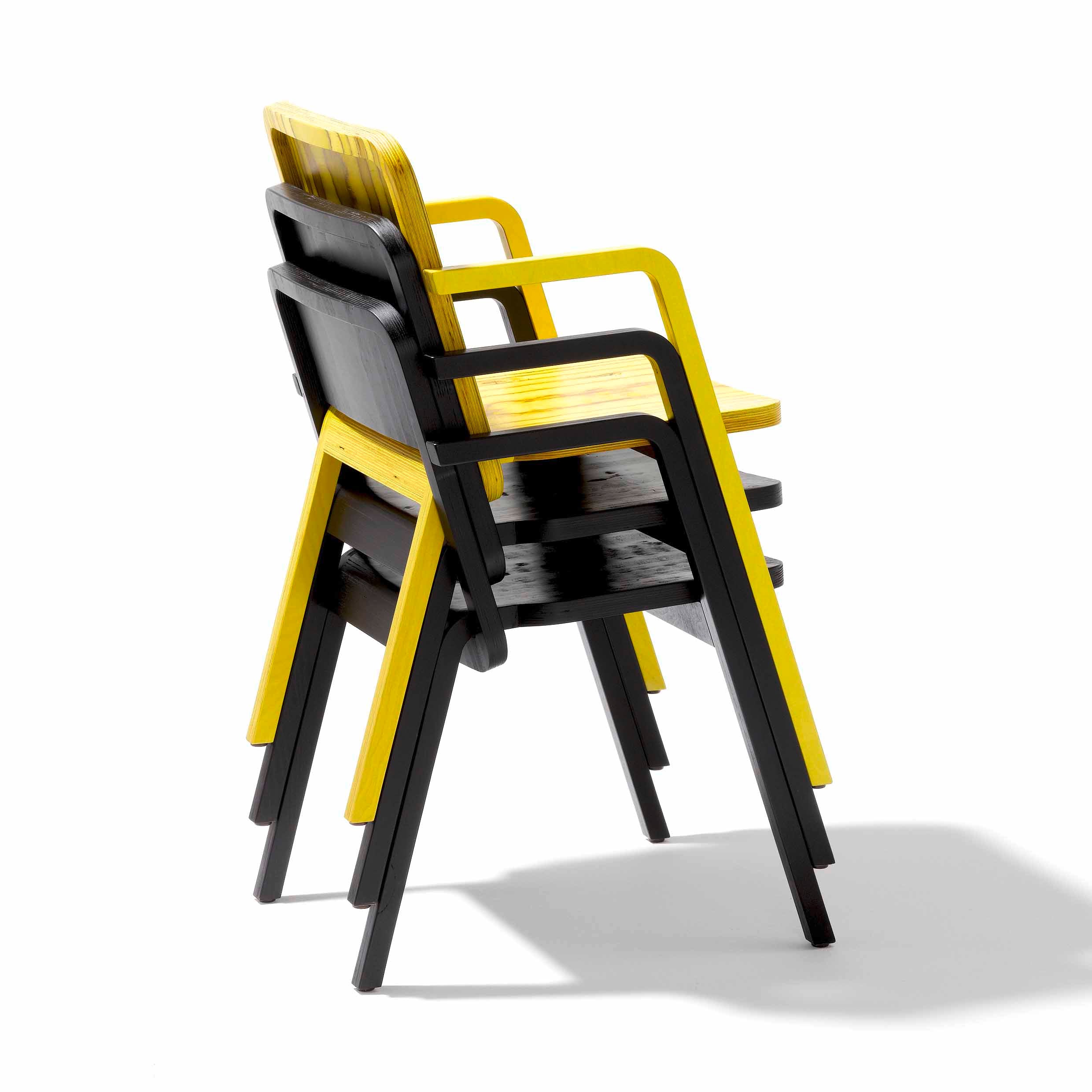Three Richard Lampert Prater Chairs display sleek CNC milling with stackable, modern design. The black seats and frames highlight the two-tone color scheme, perfectly complementing the bright yellow armrests and backs as they are stacked slightly angled.
