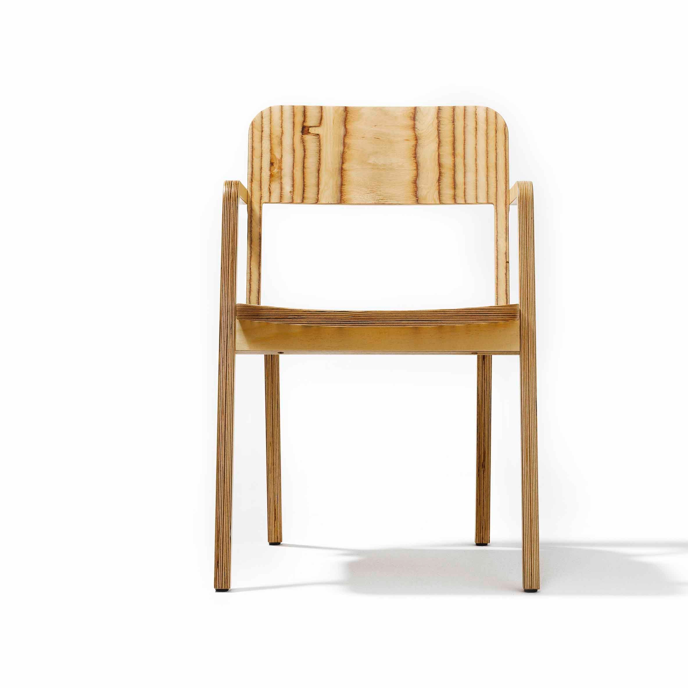 The Prater Chair by Richard Lampert showcases a front view in birch plywood with a minimalist, smooth finish and notable wood grain. It features a straight backrest with armrests, while its legs splay outward slightly.