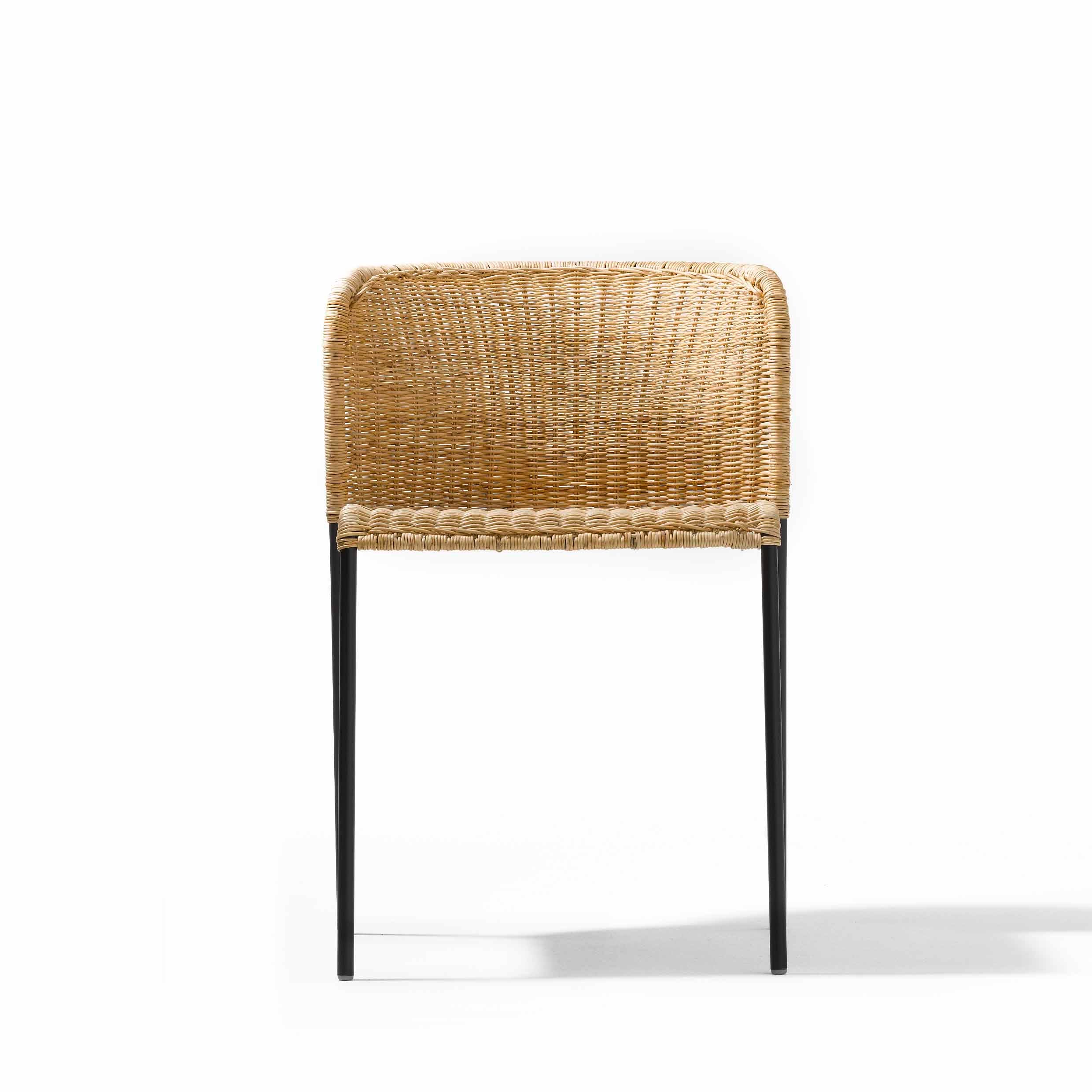 The Santa Lucia by Richard Lampert, a rattan chair featuring a rounded backrest and black metal legs, stands elegantly against a white background, echoing Bauhaus-inspired minimalist charm.