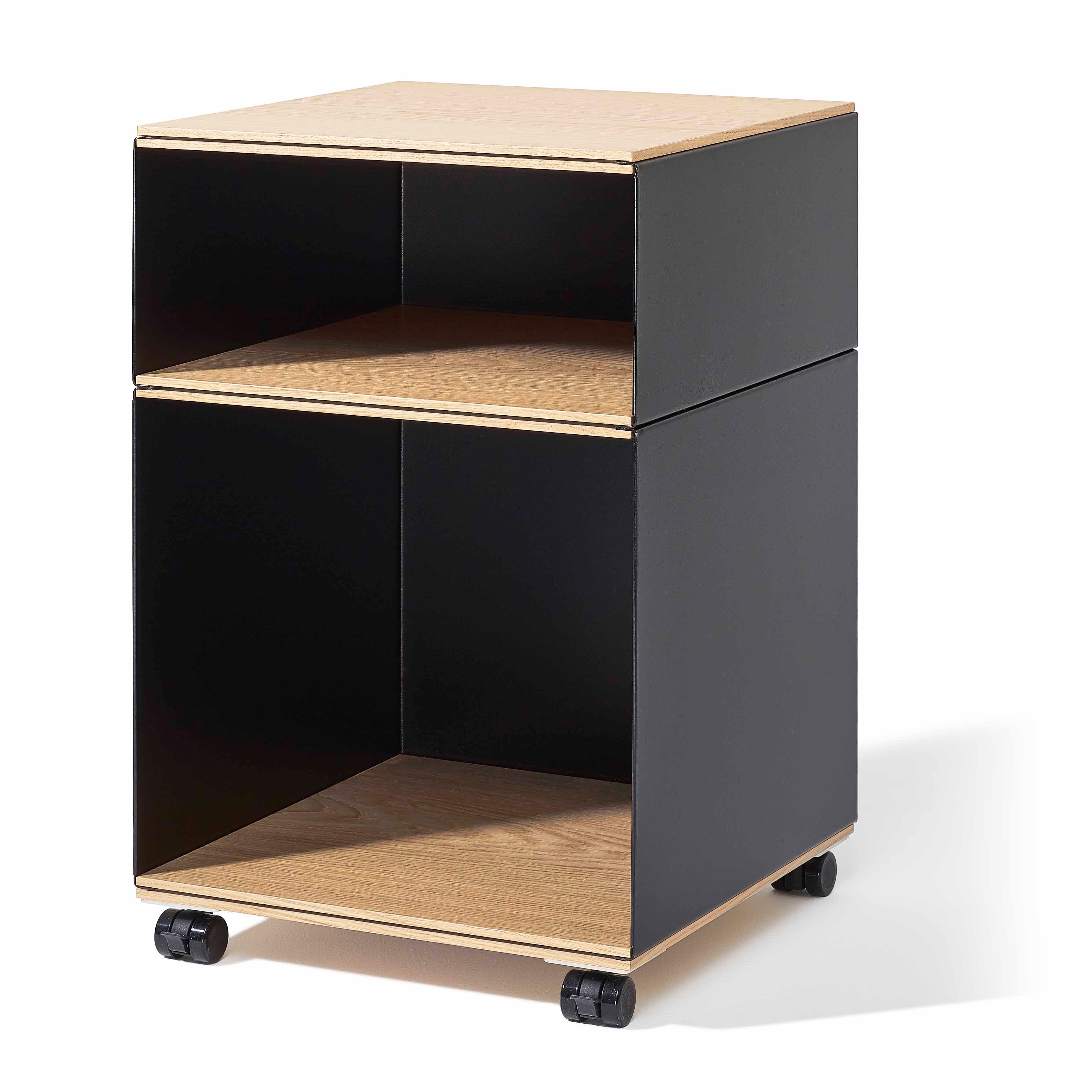 The Stak Trolley System by Richard Lampert is a mobile storage unit featuring a sleek black exterior, solid oak shelves, two open compartments, and four adjustable castors for easy movement.