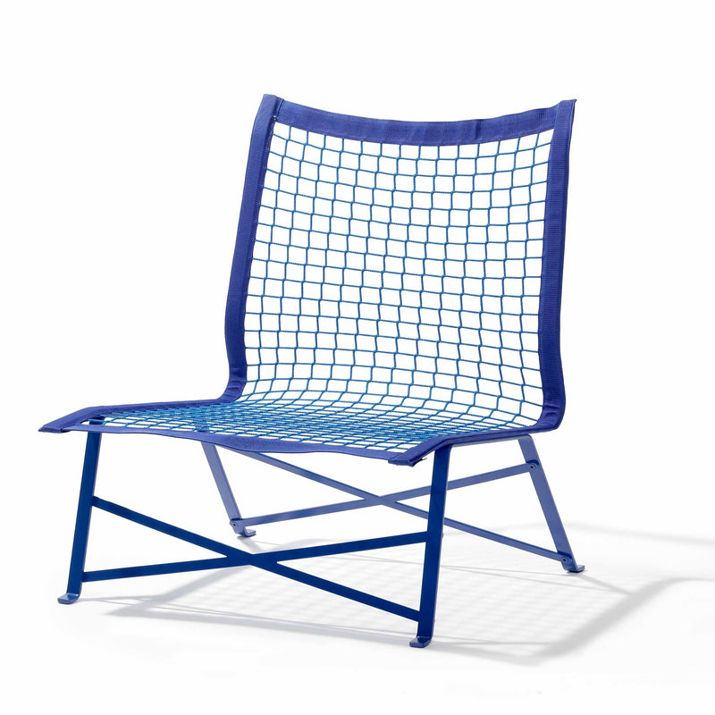 The Tie-Break Lounge Chair by Richard Lampert is a modern outdoor armchair with a blue metal frame made of flat-rolled steel and a blue netted seat and backrest. Its angular, geometric design adds a minimalist touch to any garden furniture set against a white backdrop.