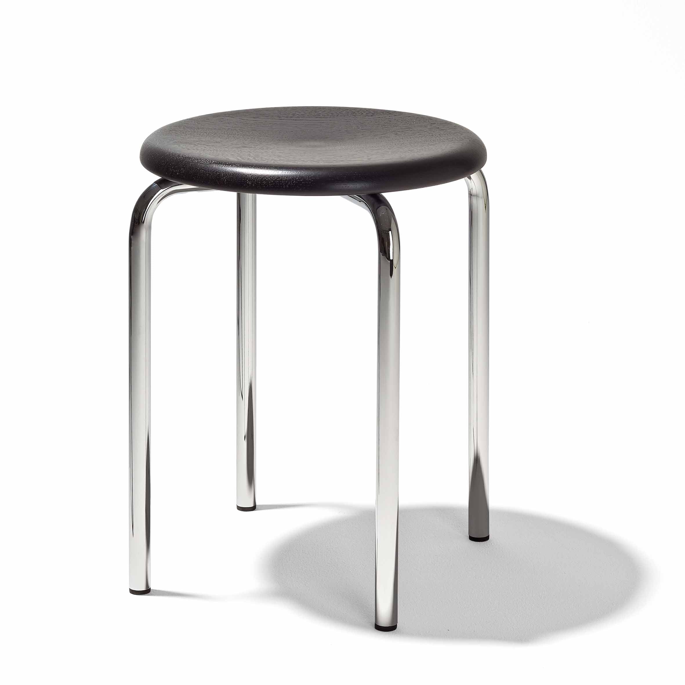The Tom Stackable Stool by Richard Lampert has a round dark wooden seat and four shiny metal legs, casting a shadow on a white background.