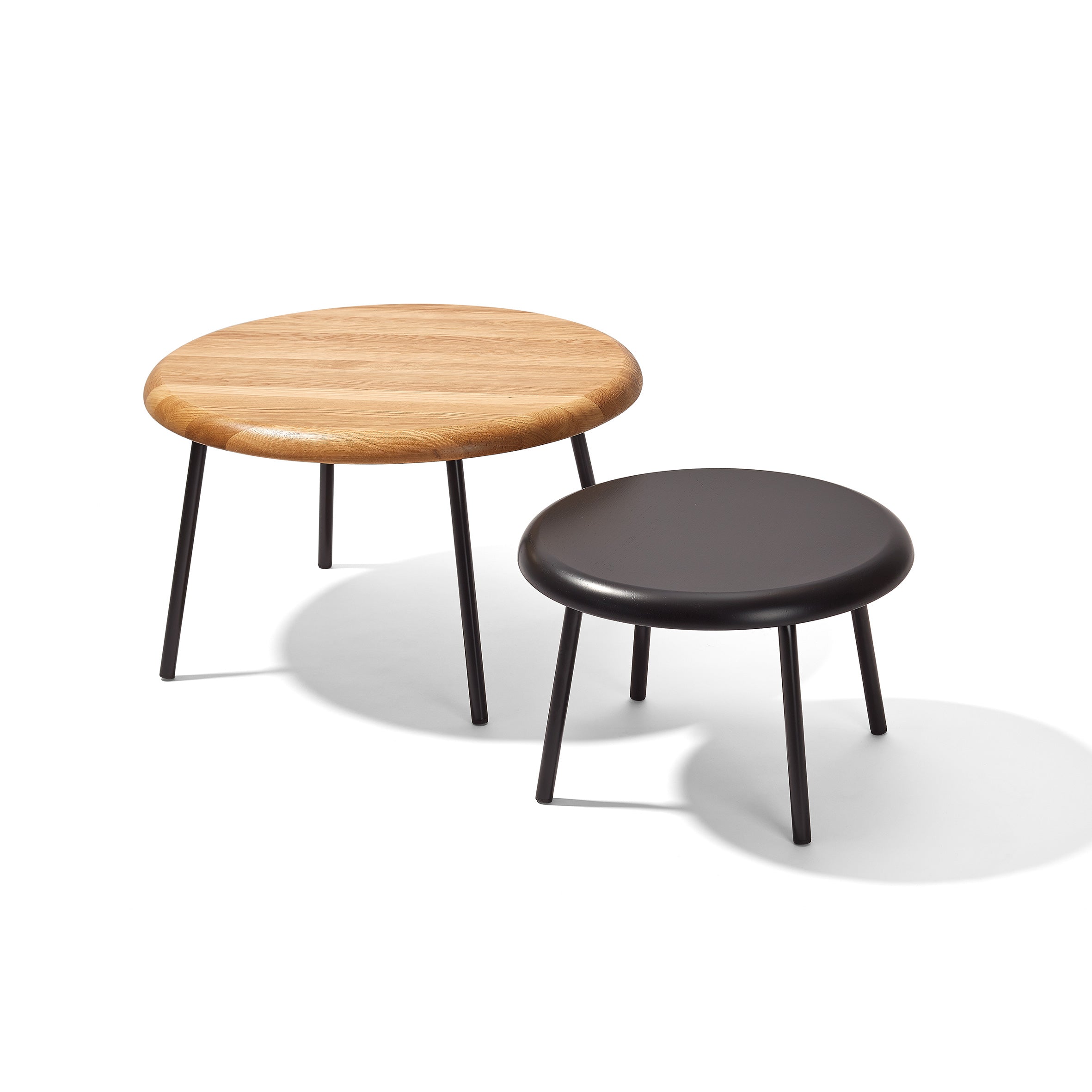 The Richard Lampert Tom Side Tables feature two round tables with tubular steel frames and black metal legs; one with a solid oak top and another with a sleek black top, both casting soft shadows on the surface below.