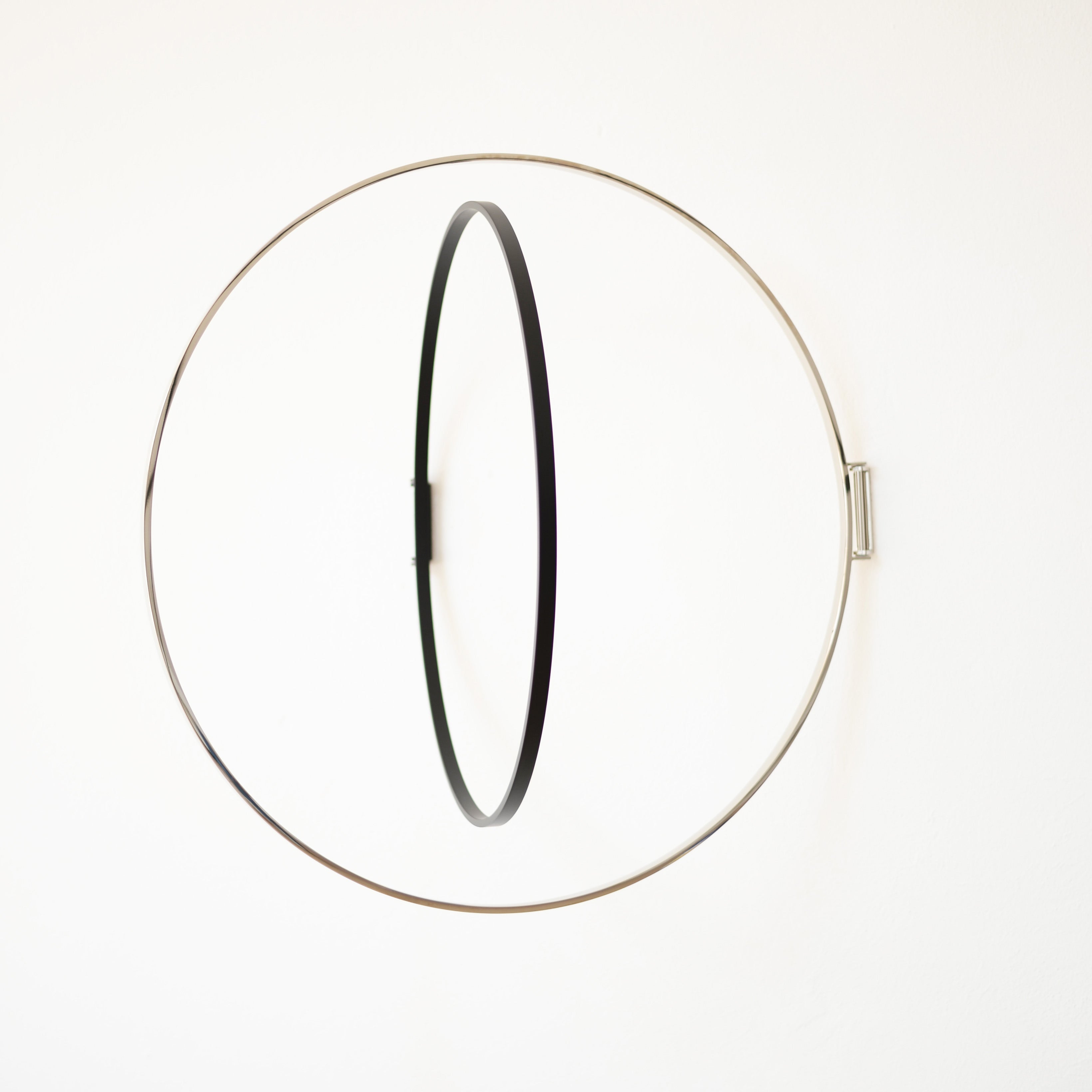Atelier Haussmanns Rings is a minimalist metal hoop art piece with a large silver ring and smaller black ring, suspended parallelly, creating depth and balance against a plain white background.