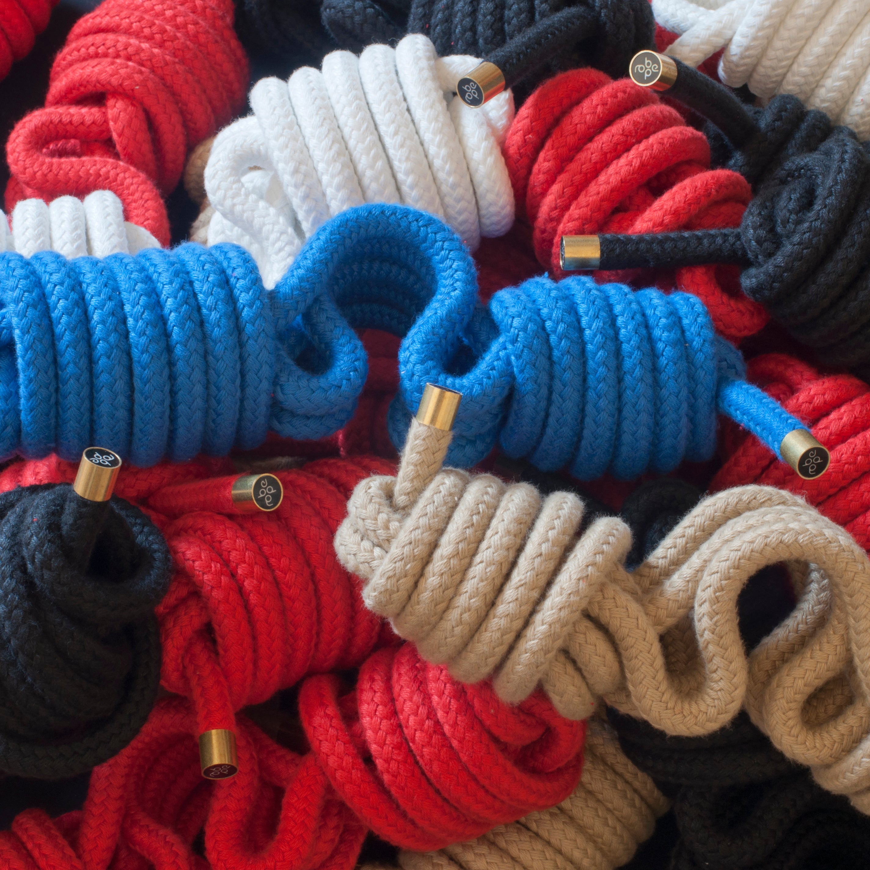 Roberope by Roberope features durable polyester yarn ropes in black, red, white, blue, and beige colors. The ropes are coiled together with metal-tipped ends to create a vibrant textured pattern that resembles an artistic display.