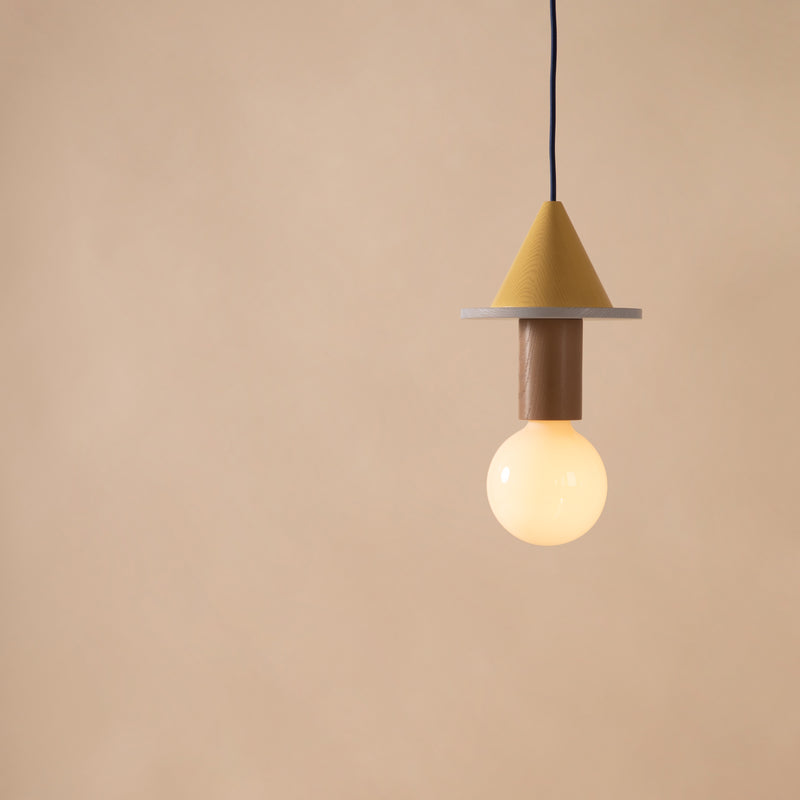 The Junit Meringe by Schneid is a Bauhaus-inspired pendant light featuring a yellow cone and round base with a glowing bulb on a black cord, set against a light brown background. Its minimalist design and soft ambient light make it ideal for contemporary spaces.