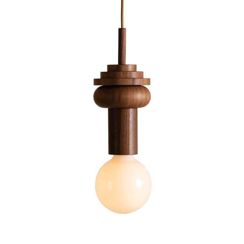 The Junit Pino by Schneid is a Bauhaus-inspired modern pendant light featuring a walnut wood tiered fixture and a glowing round bulb suspended from a cord, adding an elegant touch.