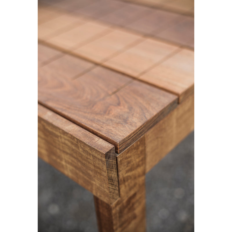 Close-up of the Egoe Sena Table corner, highlighting its checkered tabletop pattern made from tropical wood. The natural finish reveals visible grain and texture, focusing on craftsmanship and clean lines at the tables edge.