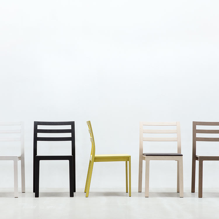 Five Hussl ST10 stackable chairs in white, black, yellow, light pink, and beige are arranged in a row against a plain white background. Featuring a modern minimalist design with horizontal slats on the backrests, they are crafted from durable wood composite.