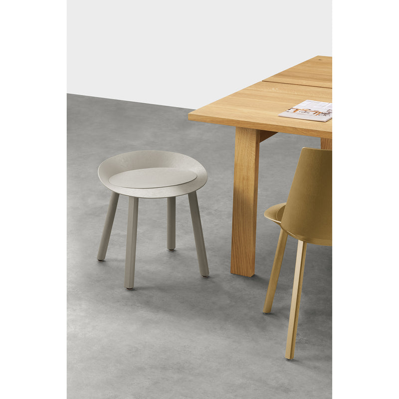 In a minimalist room, a wooden table is paired with the E15 ST13 MR. COLLINS stool for ergonomic comfort and a dynamic yellow chair on a gray floor; a magazine rests casually on the table.