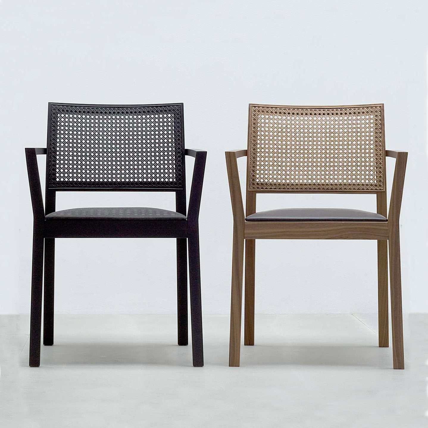 Two Hussl ST4N Gritsch Armchairs with Viennese weave backrests, one black with a dark seat and the other brown with a lighter seat, sit side by side against a plain light wall. This minimalist coffeehouse furniture piece exudes charm.