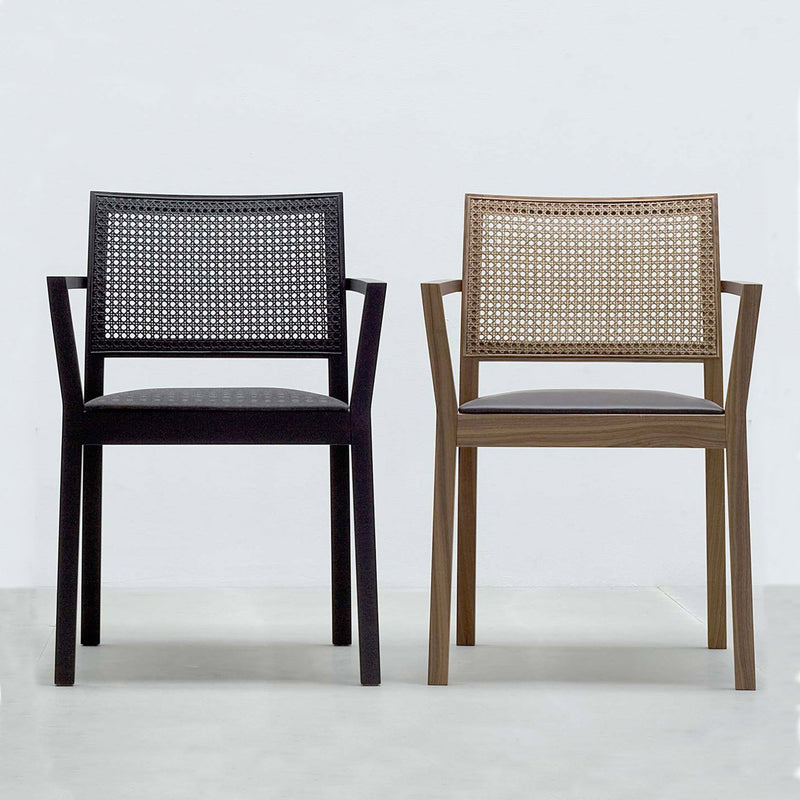 Two Hussl ST4N Gritsch Armchairs with Viennese weave backrests, one black with a dark seat and the other brown with a lighter seat, sit side by side against a plain light wall. This minimalist coffeehouse furniture piece exudes charm.