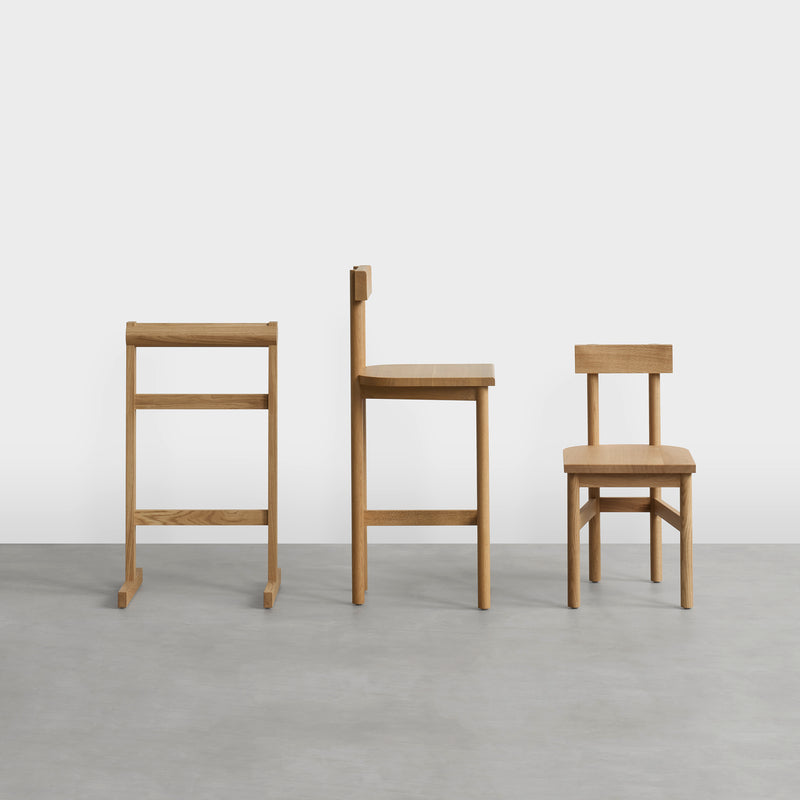 Three E15 SX02 GAMAR BARSTOOL chairs, made from European oak, sit in a row on a concrete floor. The left chair is the tallest and narrowest, while the right is shortest with a wider backrest against a plain white background.