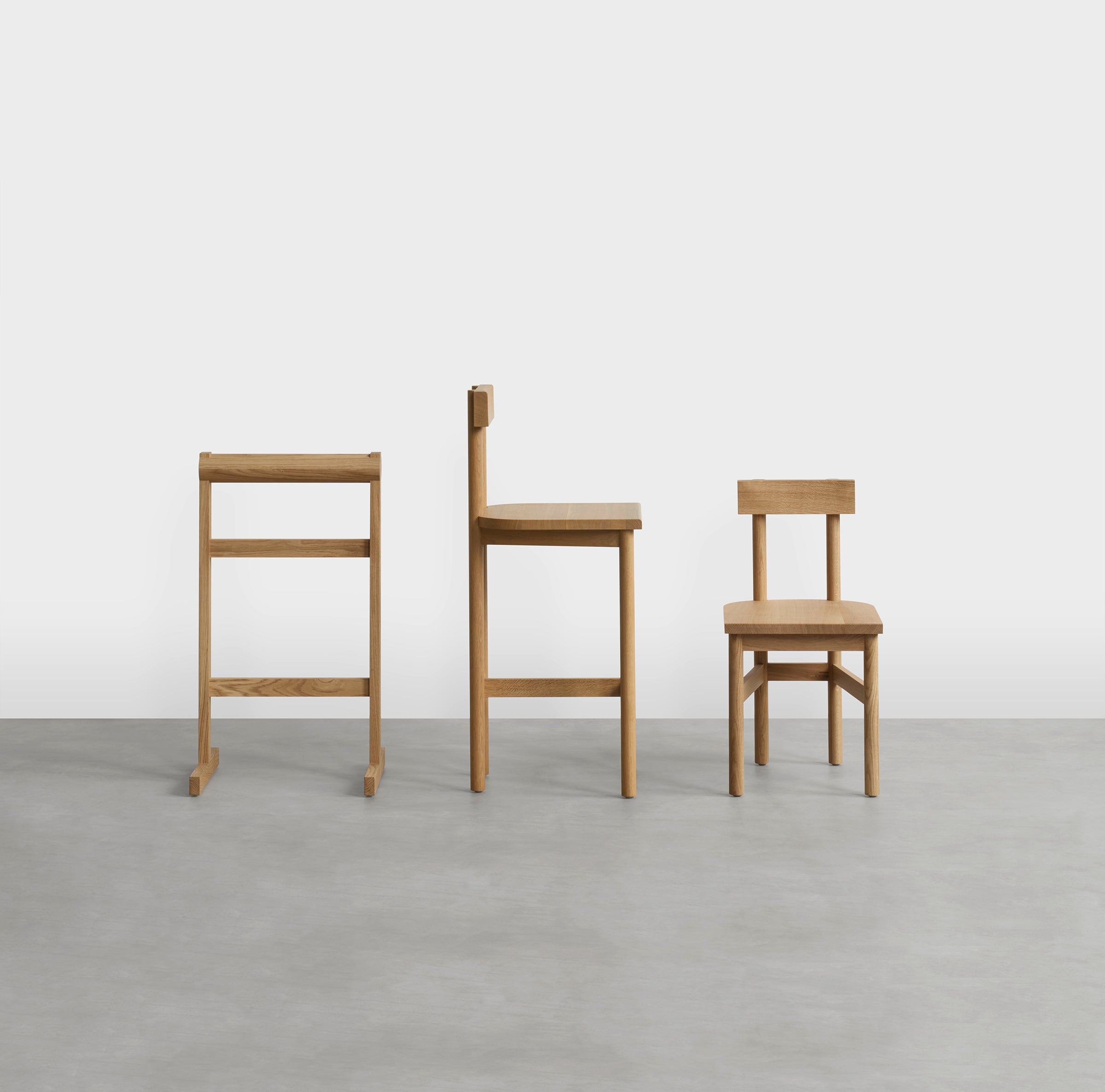 Three E15 wooden childrens chairs from the SX03 GAMAR Wardrobe Stand series sit on a smooth light gray floor against a white backdrop. The chairs feature a modern rustic design with straight lines and are crafted from European oak, each with different heights and styles.