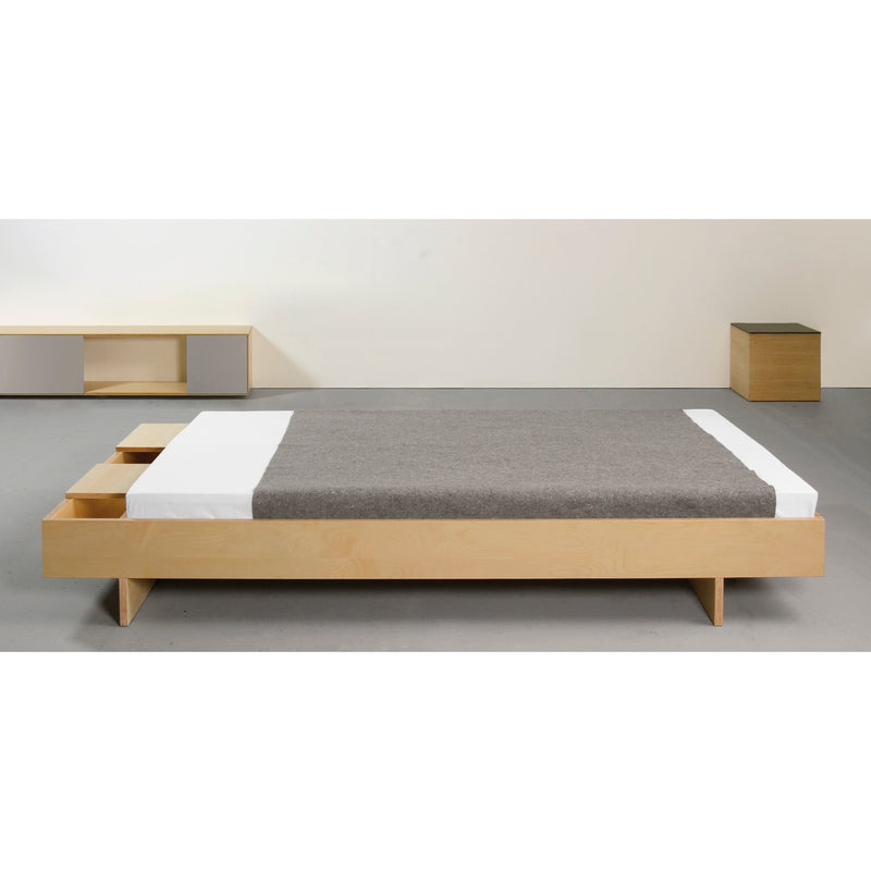 A minimalist bedroom features a Sanktjohanser Bezwei Bed with a wooden platform and gray blanket over white sheets. Two rectangular nightstands enhance the design, providing a sleek, modern look with customizable dimensions for personalized comfort.