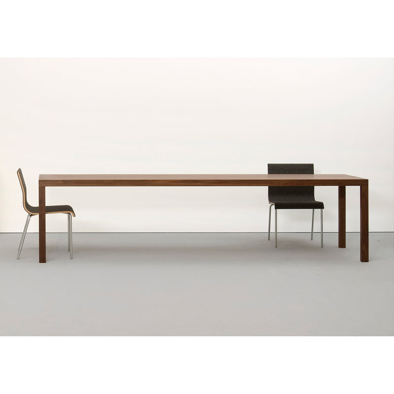 In a minimalist scene, the Sanktjohanser Dinavier Table, known for its detachable legs and solid wood design, is styled with two chairs at each end. A white background and floor enhance the simplicity of this long, rectangular table.