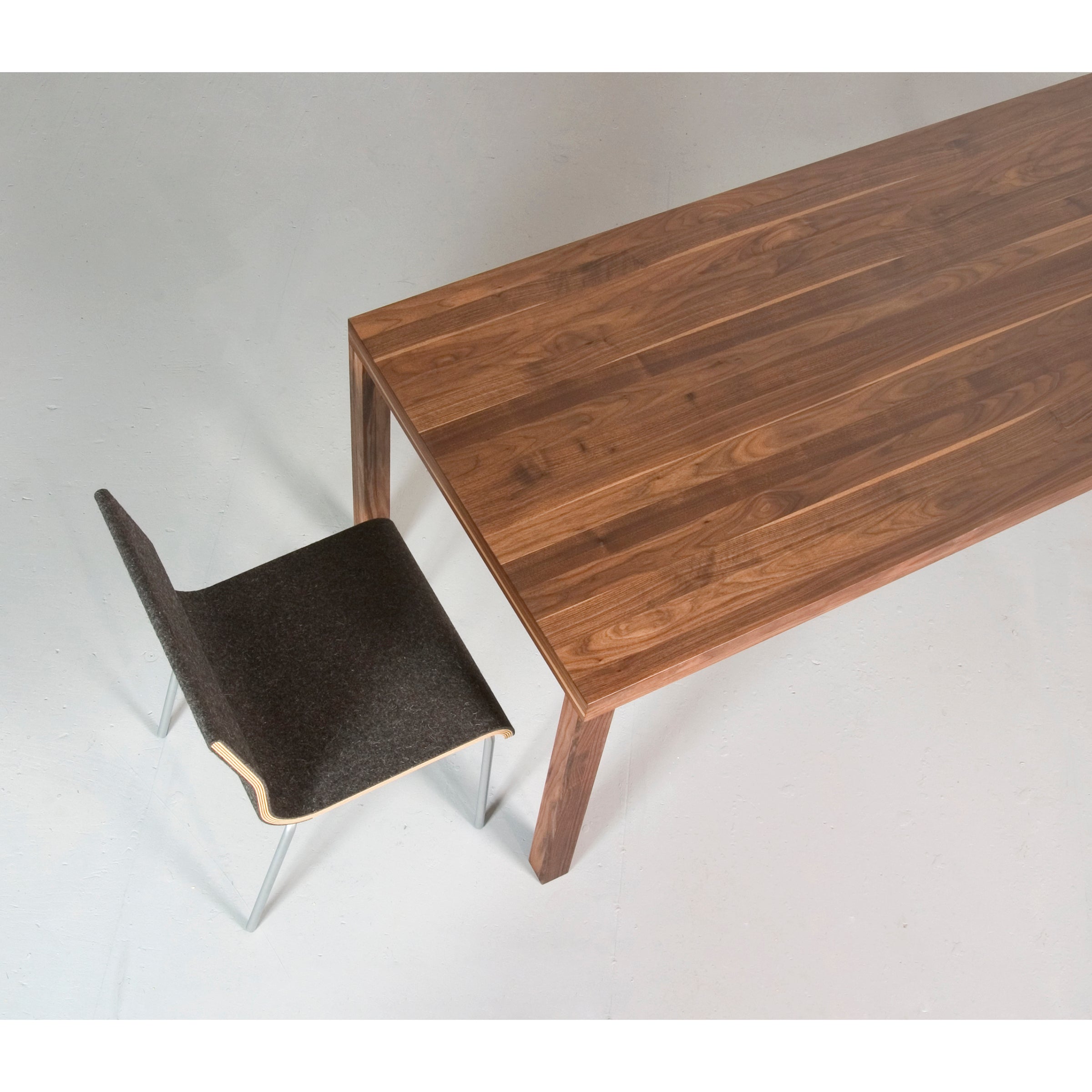 A top view of the Sanktjohanser Dinavier Table highlights its brown grain solid wood design. Nearby, a modern chair with a textured dark upholstered seat and metal legs is seen partially on a light smooth floor, alongside the tables detachable legs.