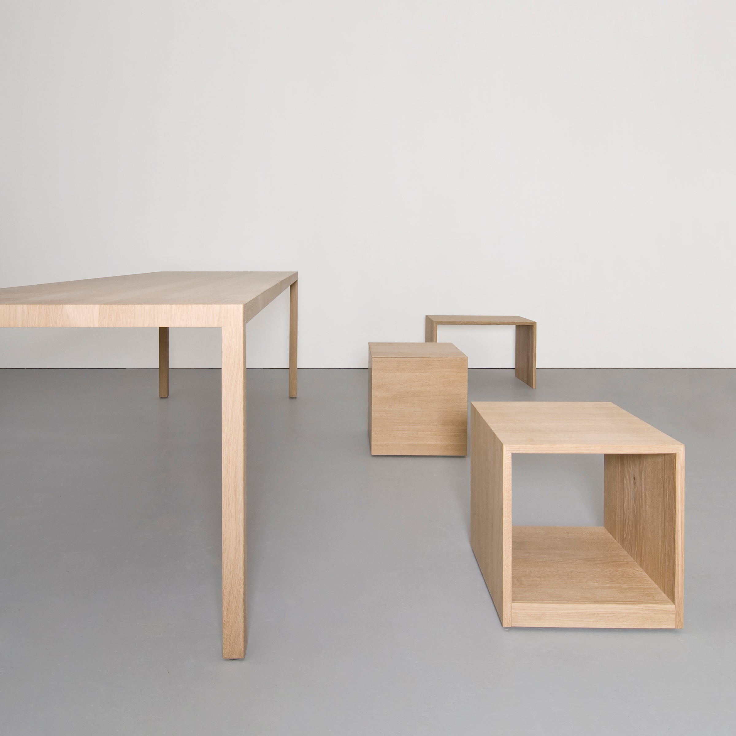 The Sanktjohanser Dinanull Table, along with cube stools and a matching low table, is elegantly arranged on a sleek gray floor against a simple white backdrop.