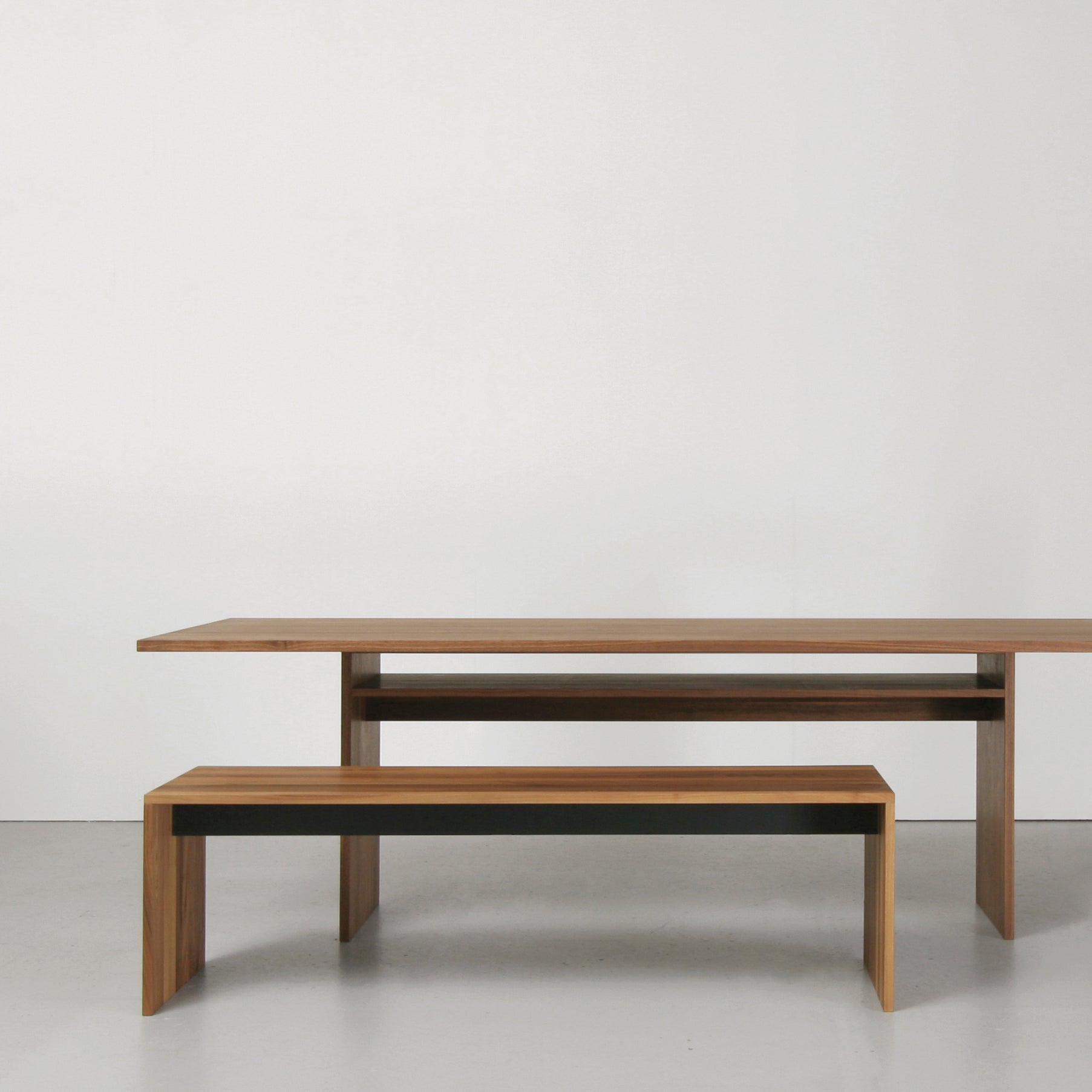 The Sanktjohanser Format Bench and matching long wooden table feature clean lines and a natural finish, set against a white wall and light gray floor. This minimalist, modern design emphasizes the elegance of the material finishes.