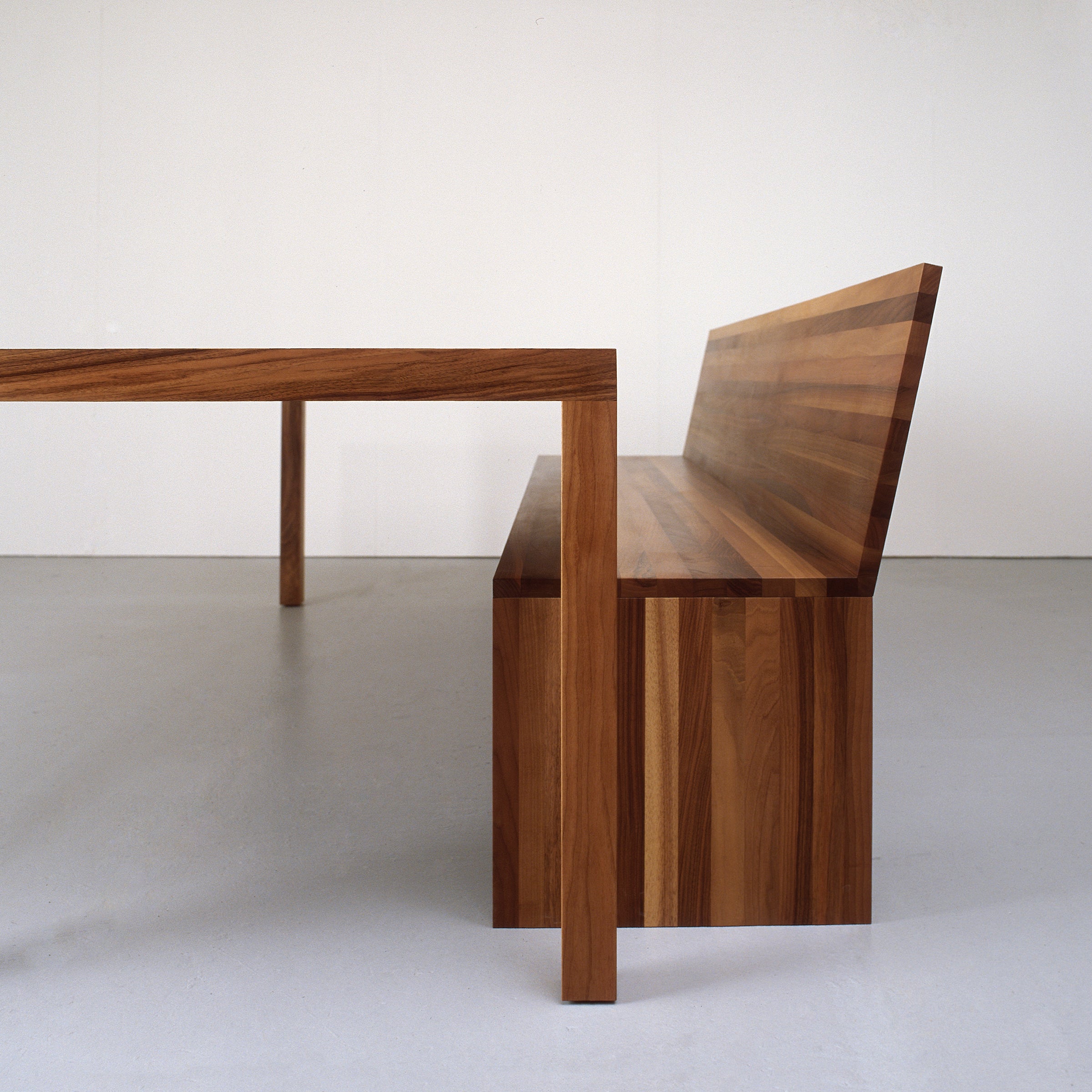 Side view of the Sanktjohanser Format Bench with matching minimalist wooden dining table, featuring a striped wood pattern. Both set against a white background, showcasing their natural finish and simple design.