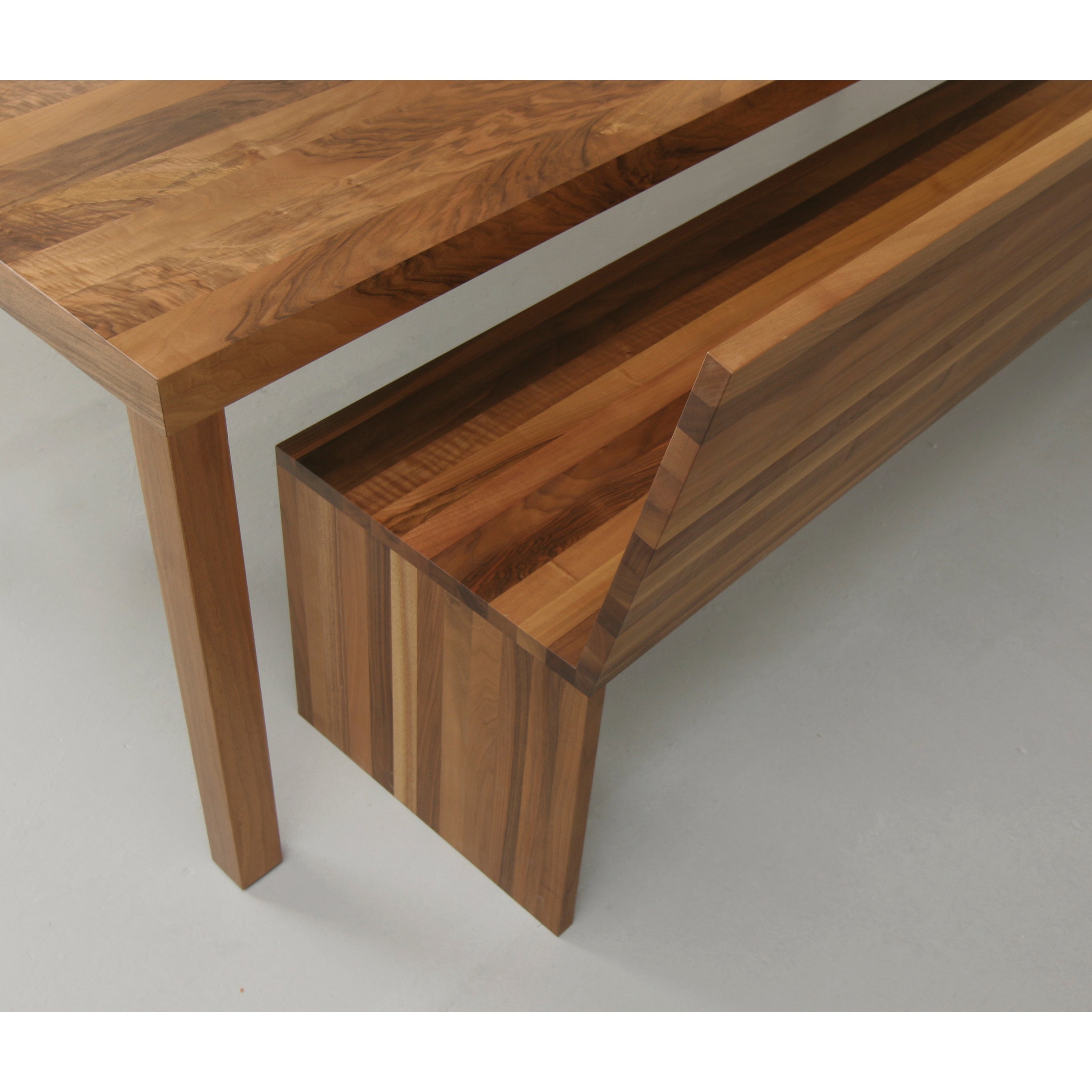 The Format Bench by Sanktjohanser is a wooden bench showcasing warm, natural wood grain and minimalist design, complemented by exquisite material finishes, set beneath a matching table against a crisp white background.