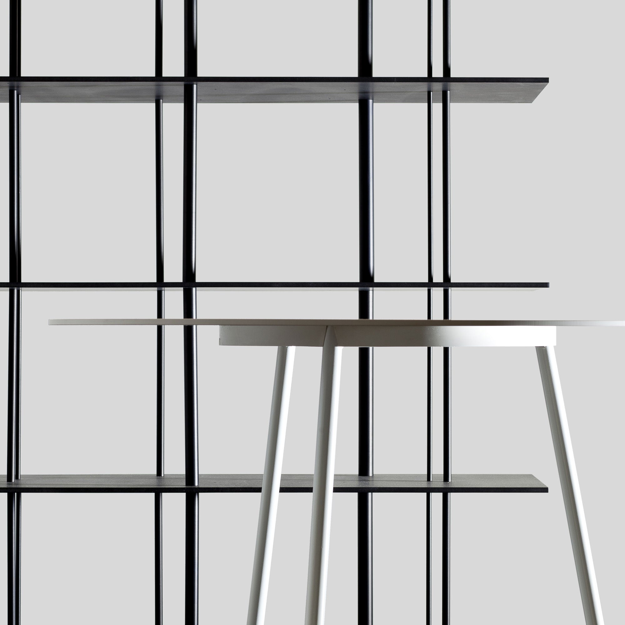 A minimalist image displays a white table with thin legs next to the Sanktjohanser Linux shelf, known for its grid pattern. Both pieces stand against a plain gray background, achieving a sleek, modern look.