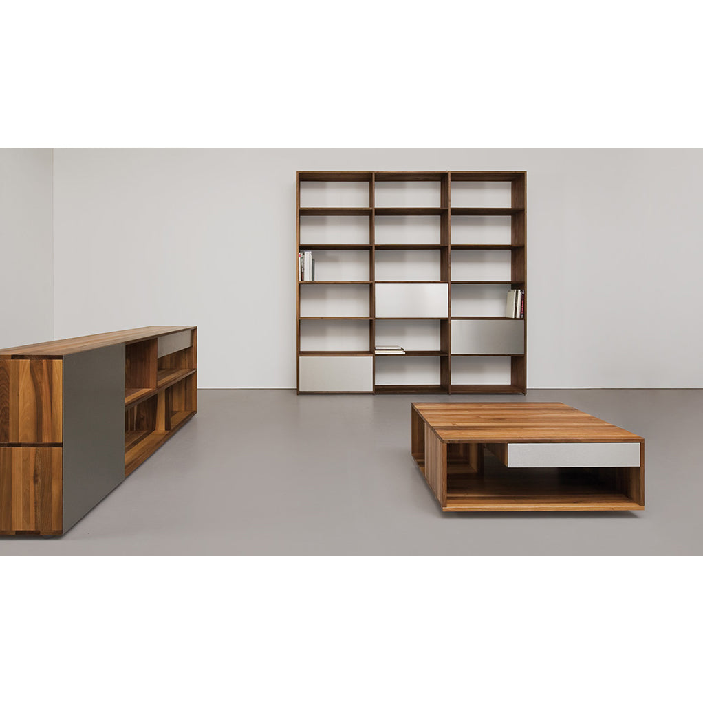 A minimalist room showcases a solid wood bookshelf, Loft coffee table by Sanktjohanser, and a side console with white accents. The open space, complemented by light gray flooring, embodies a clean and modern aesthetic.