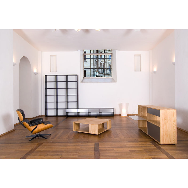 In this minimalist living room with hardwood floors, a black and tan lounge chair complements a Sanktjohanser Loft coffee table. A large shelving unit with black and white squares adds structure, while abstract patterns dance across the wall from the windows reflections.