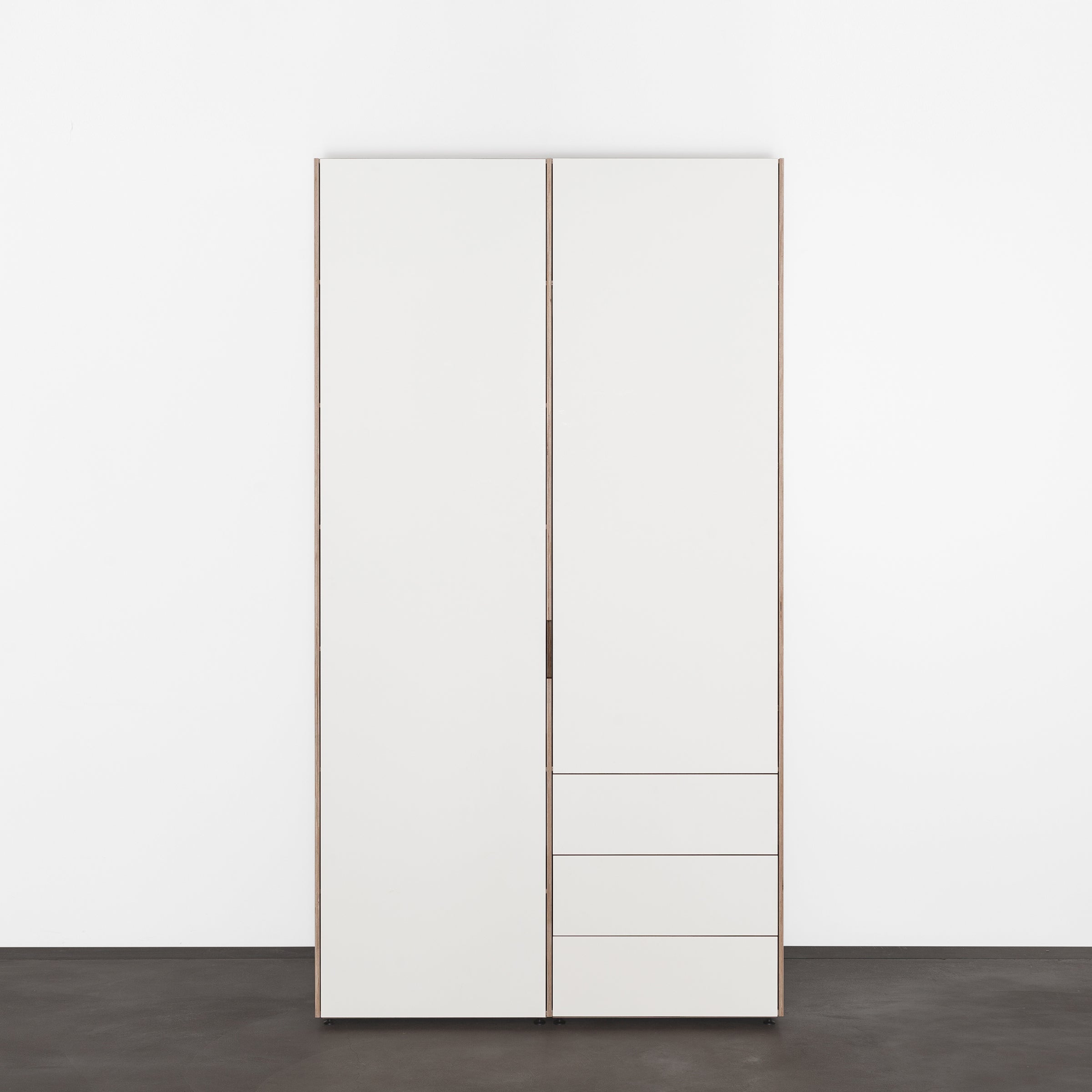 The Metrum Storage by Sanktjohanser is a sleek, minimalist cabinet with two tall doors and four small drawers on the lower right. This custom white wardrobe stands elegantly against a plain white background, serving as an exceptional storage system.