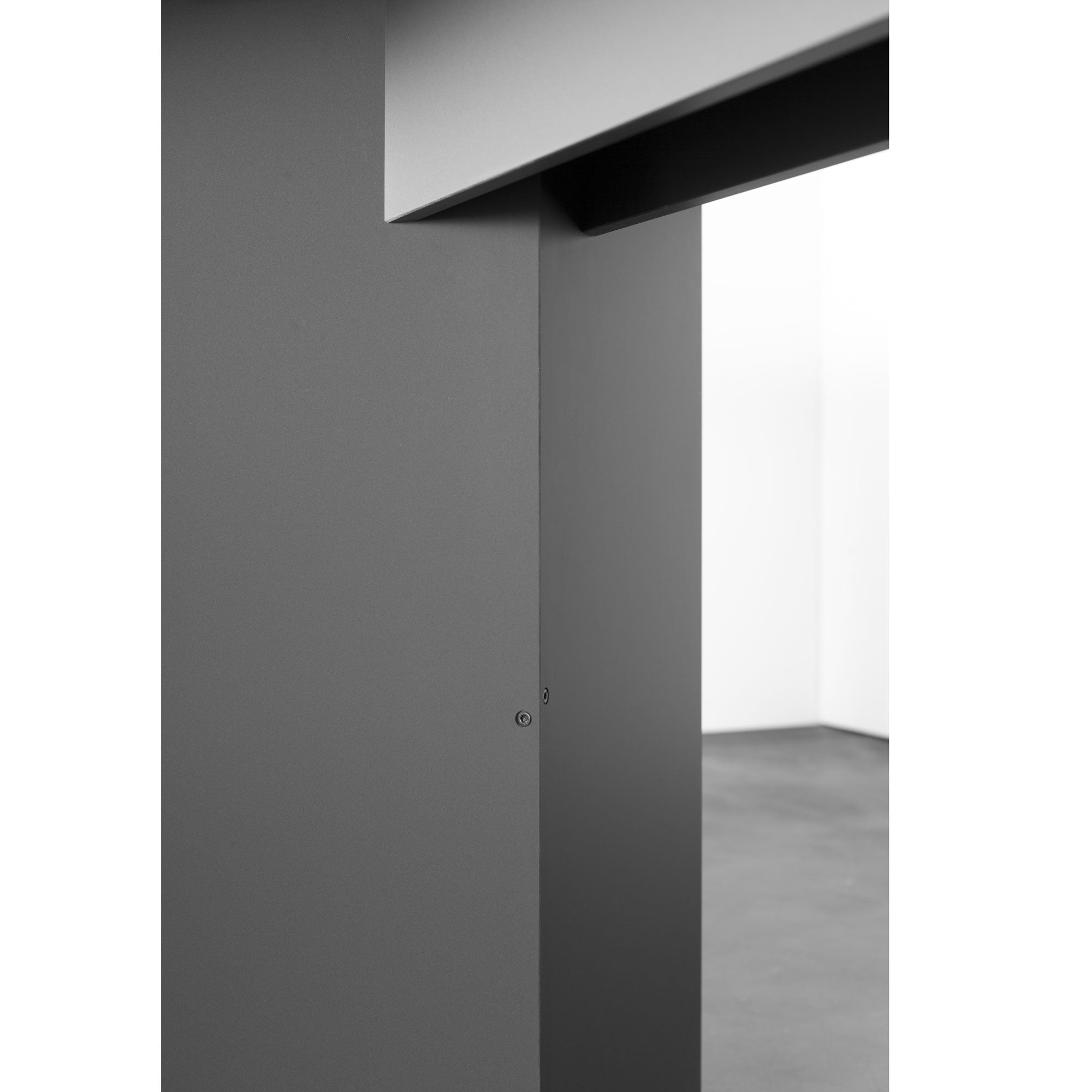 A minimalist architectural interior with gray geometric walls showcases sharp angles and clean lines. A Sanktjohanser Mono Table complements the space, enhancing its modern and abstract feel with customizable design options that play with contrasting light and shadow.