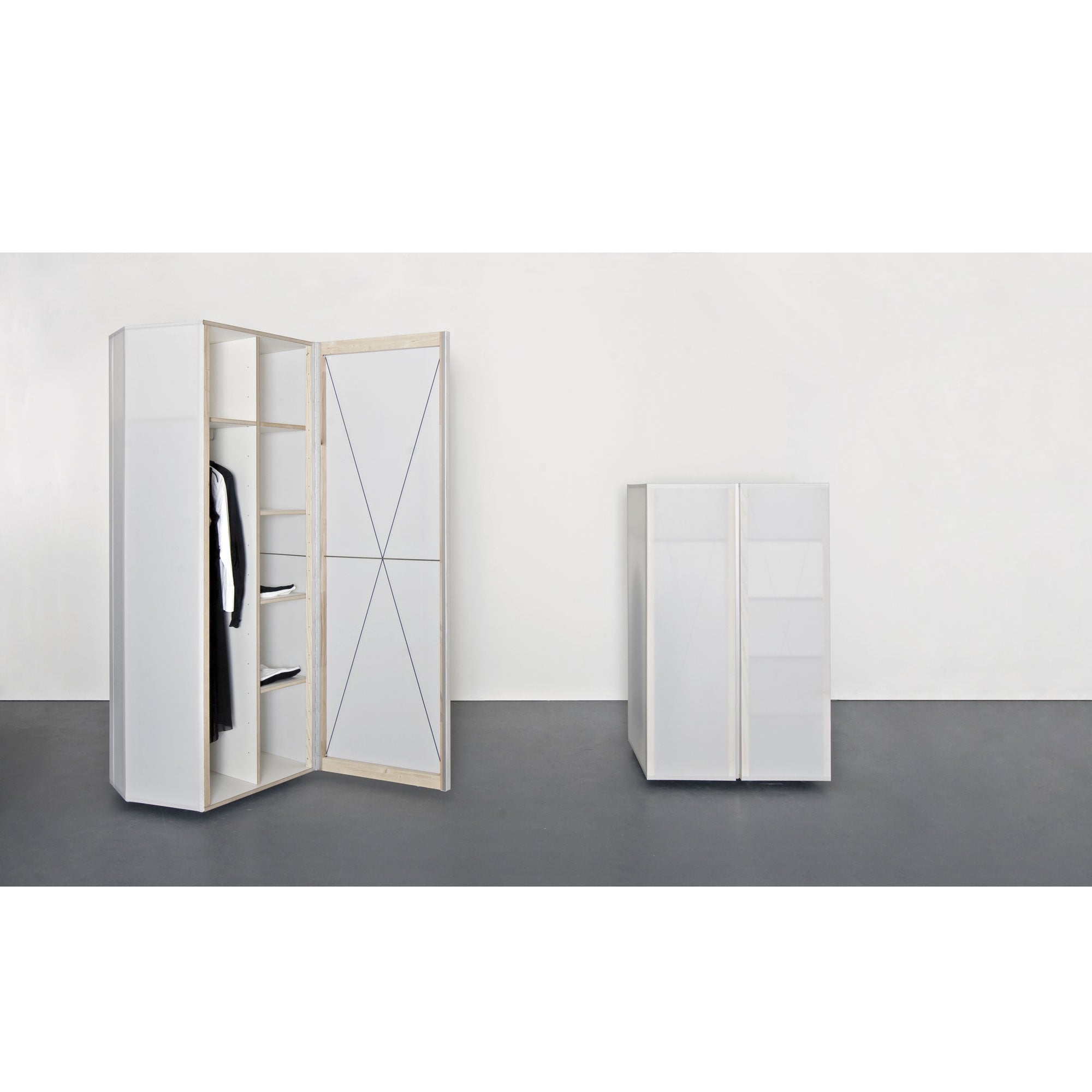 Two Quartier wardrobes by Sanktjohanser, one framed with solid oak, stand against a plain wall. The left wardrobe has an open door showing shelves, a hanging rail with a black garment, and a mirror with geometric lines. The right one is closed and slightly shorter.