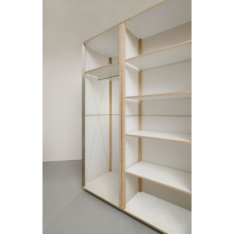 The Quartier wardrobe by Sanktjohanser is a minimalist unit featuring solid oak frame with white panels, combining open shelves and hanging space. The rooms neutral gray floor and off-white walls enhance its clean, modern appearance.