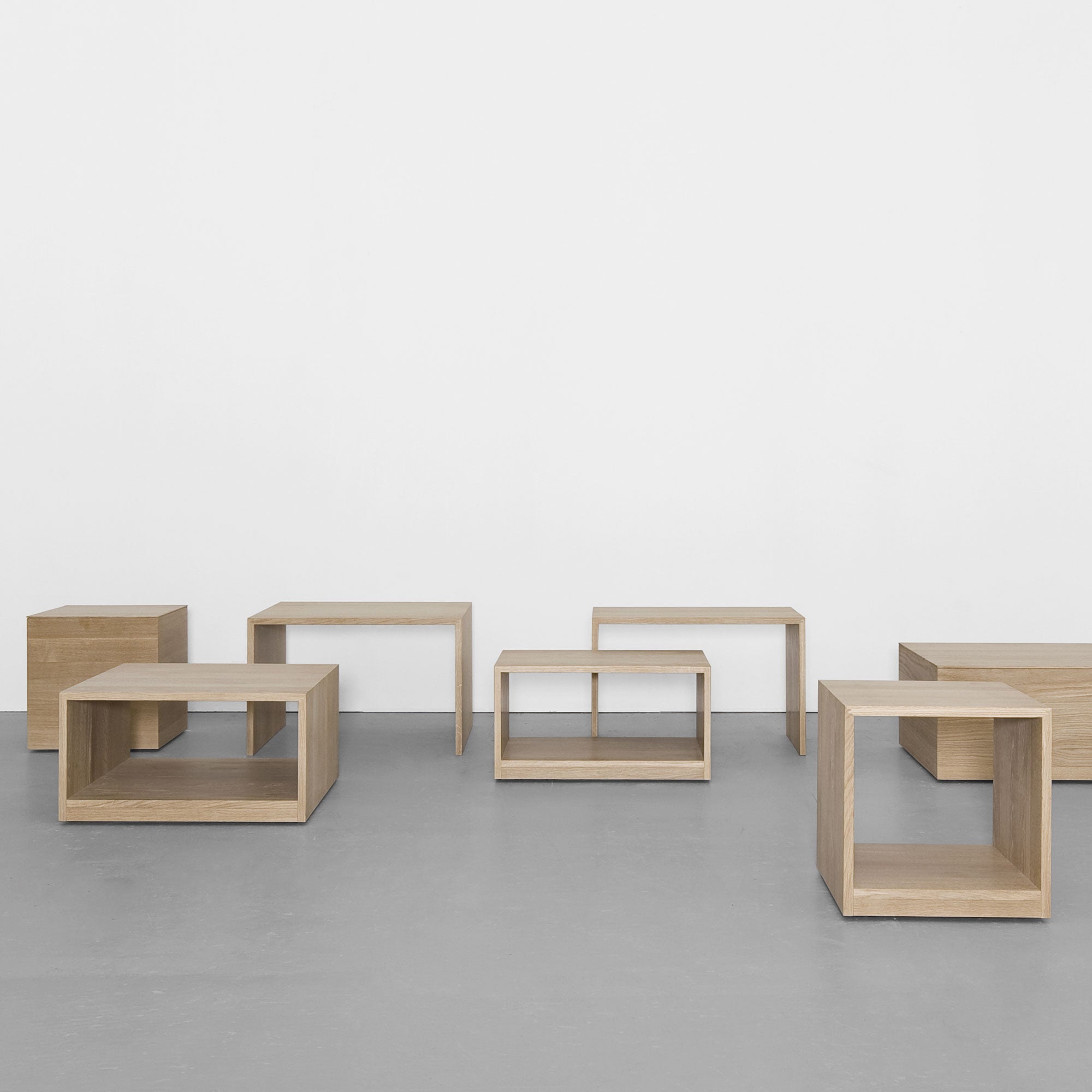 Sanktjohansers Relikt multipurpose tables and open cubes form a clean, modern geometric display on a smooth gray floor against a plain white wall, evoking minimalist modular furniture.