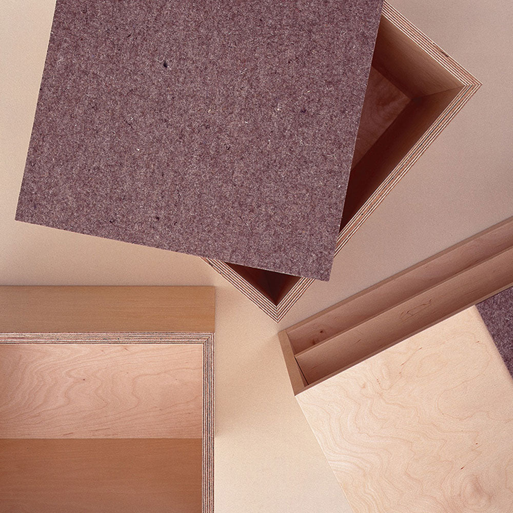 Social Cube by Sanktjohanser features open wooden boxes with brown felt lids, showcased on a light surface. A partially removed lid reveals the interior, highlighting a minimalist design in light-colored wood, hinting at its versatility as multi-purpose furniture.