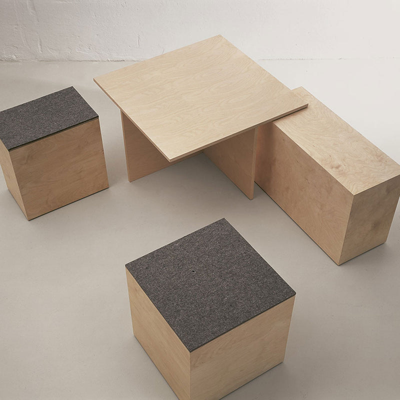 The Sanktjohanser Social Cube is a minimalist furniture set with a light wooden finish. It includes a rectangular table and three cube stools with dark gray cushions, all featuring clean lines. Ideal for multi-purpose use, this versatile set complements any light-colored floor.